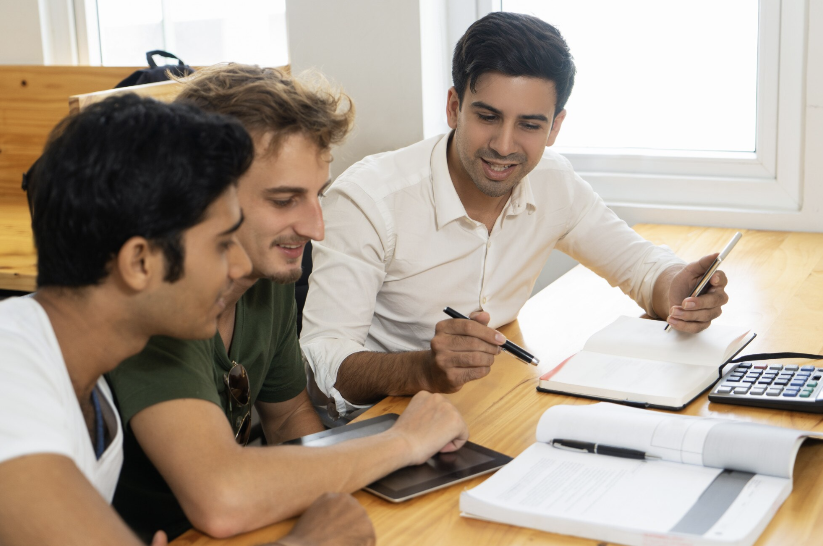 tres chicos estudiando con libros calculadora y una tablet