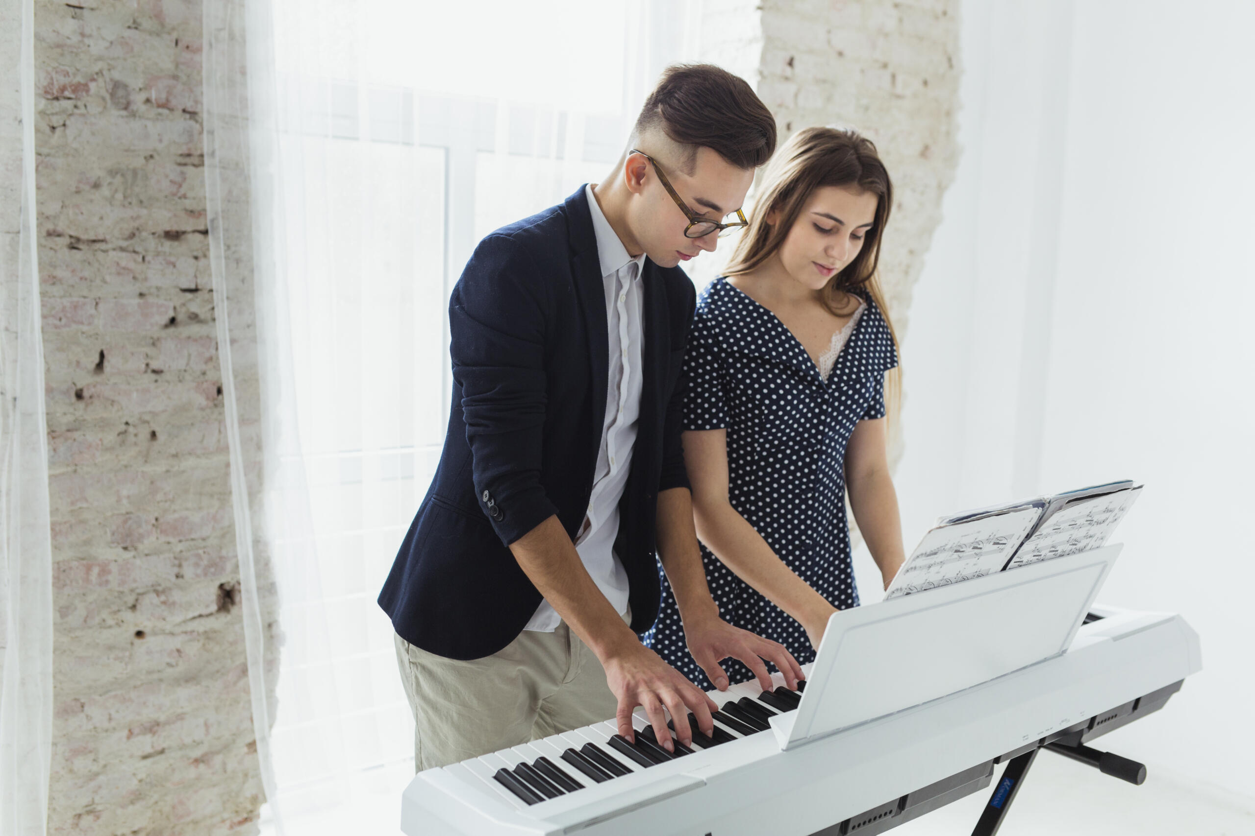 chico y chica tocando un teclado eléctrico a la vez mientras leen las partituras