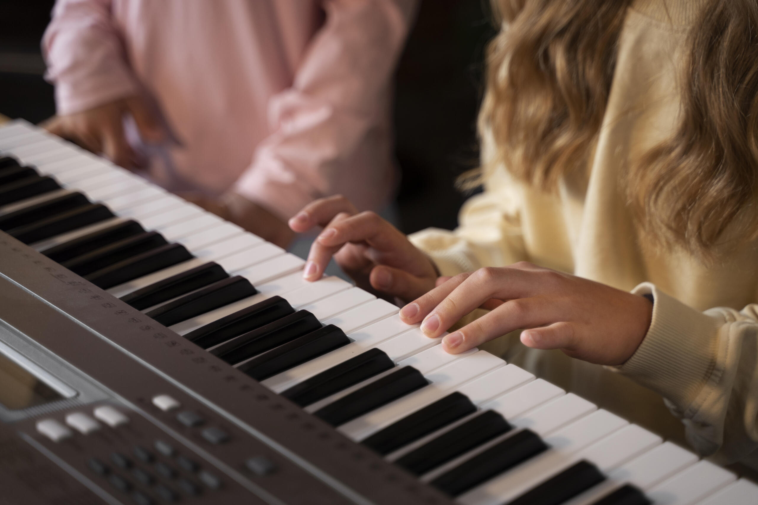 vista detalle de un teclado electrónico con manos de una niña tocando mientras otra persona está junto a ella