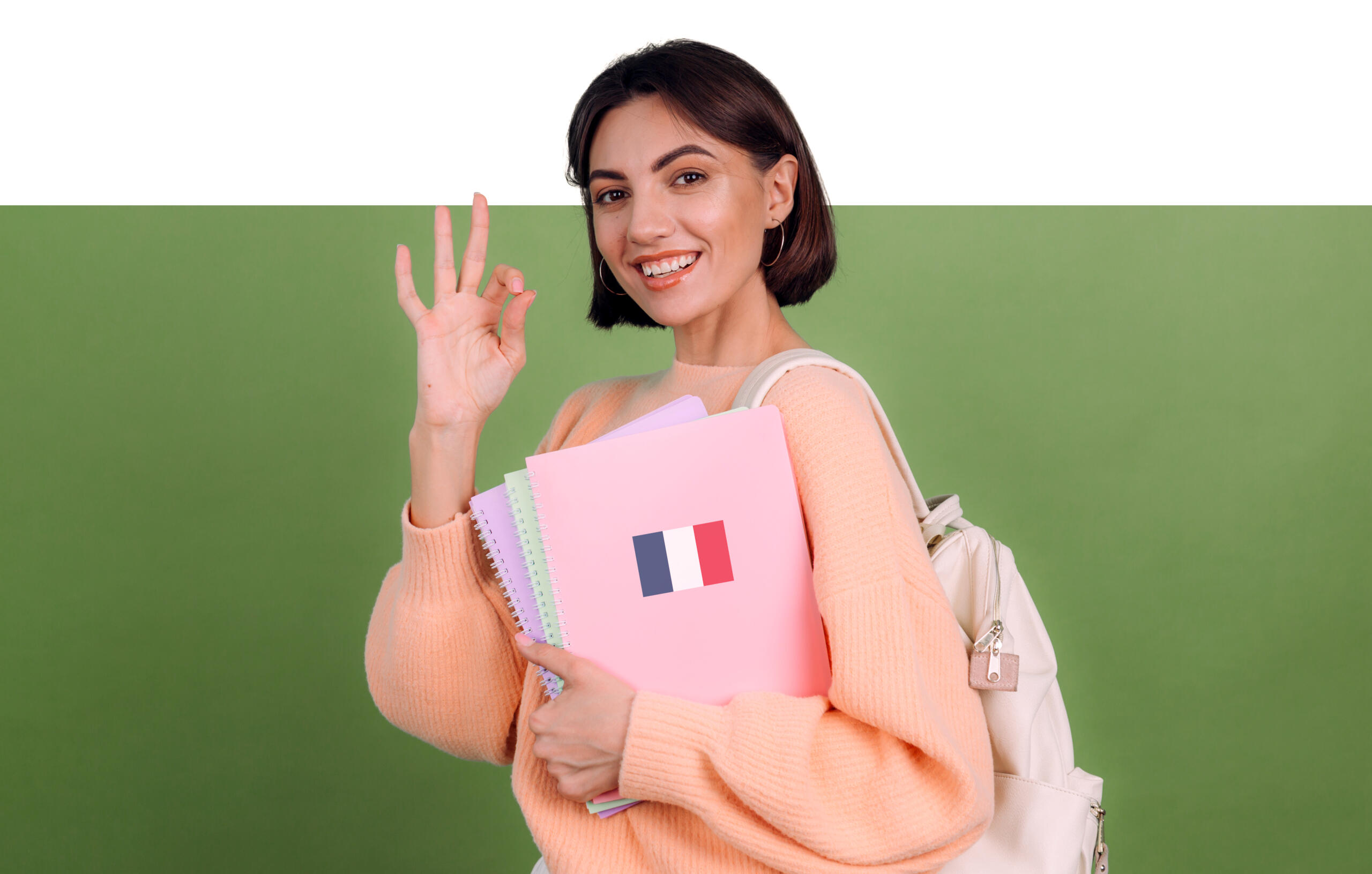 chica con sus libros de frances en una mano y con la otra, haciendo un ok sonriente mirando a la cámara