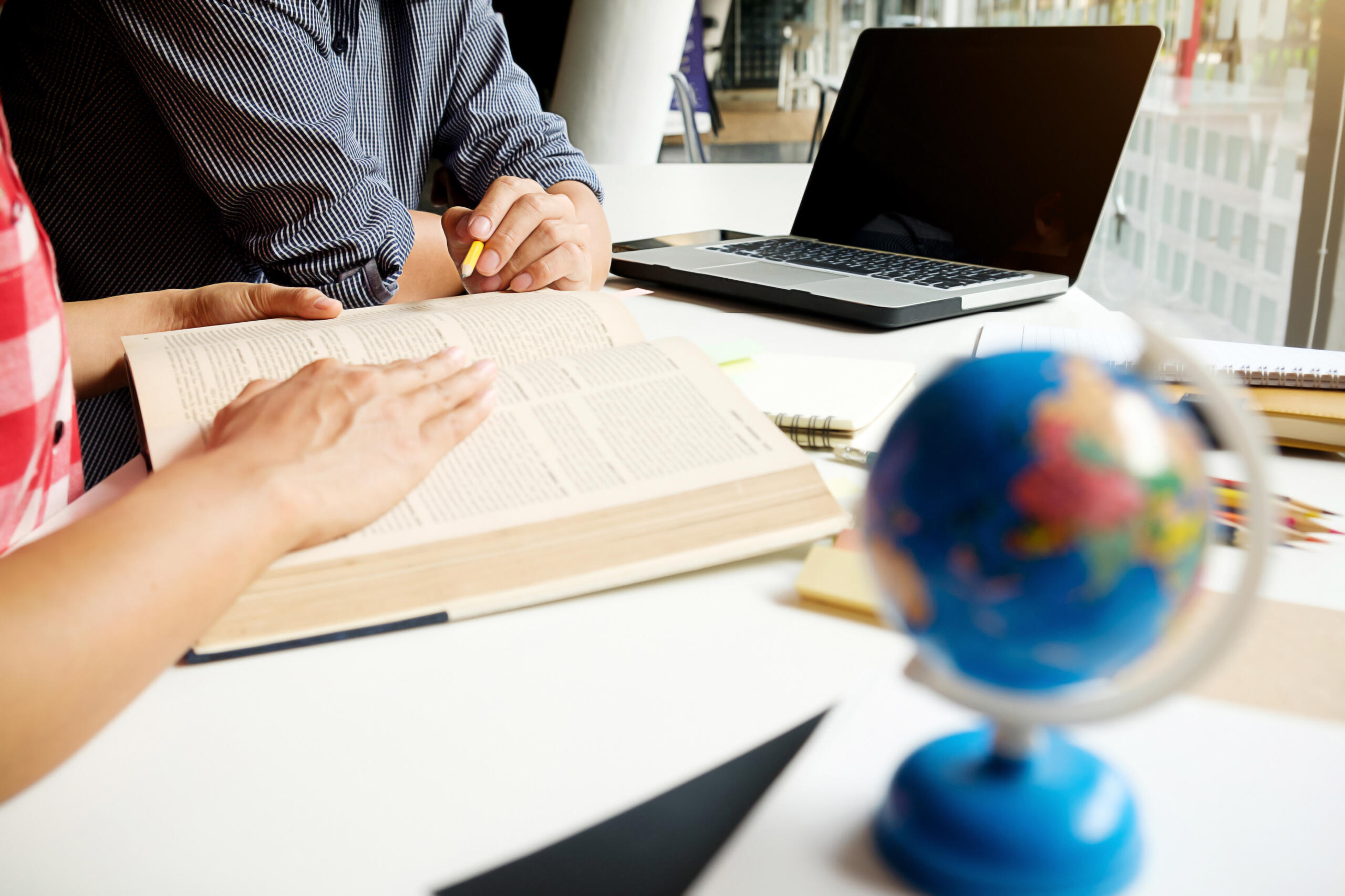 toma detalle de dos personas estudiando con un globo terráqueo en primer plano