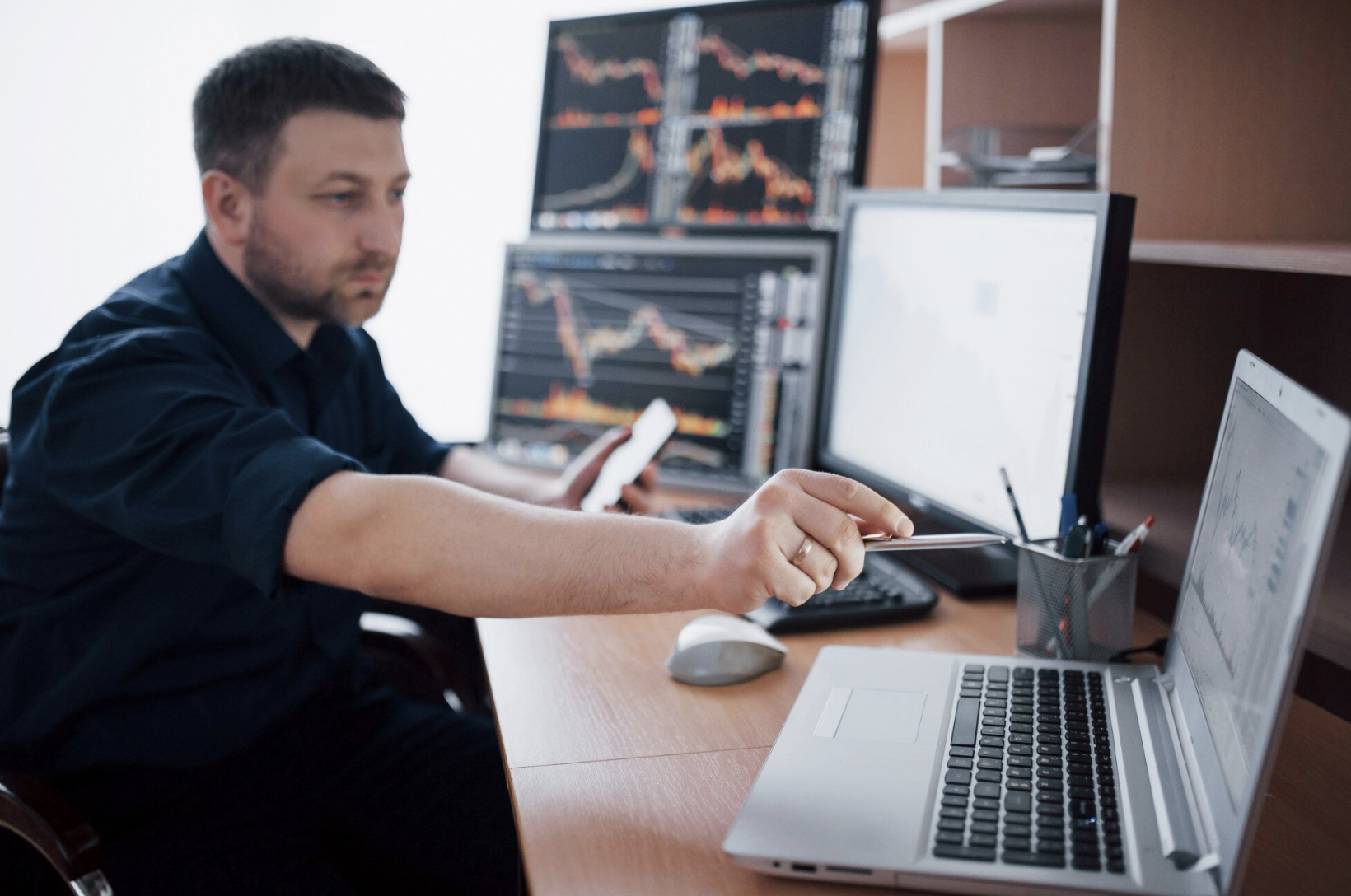 joven sentado en medio de computadoras analizando diagramas de flujos de diferentes inversiones