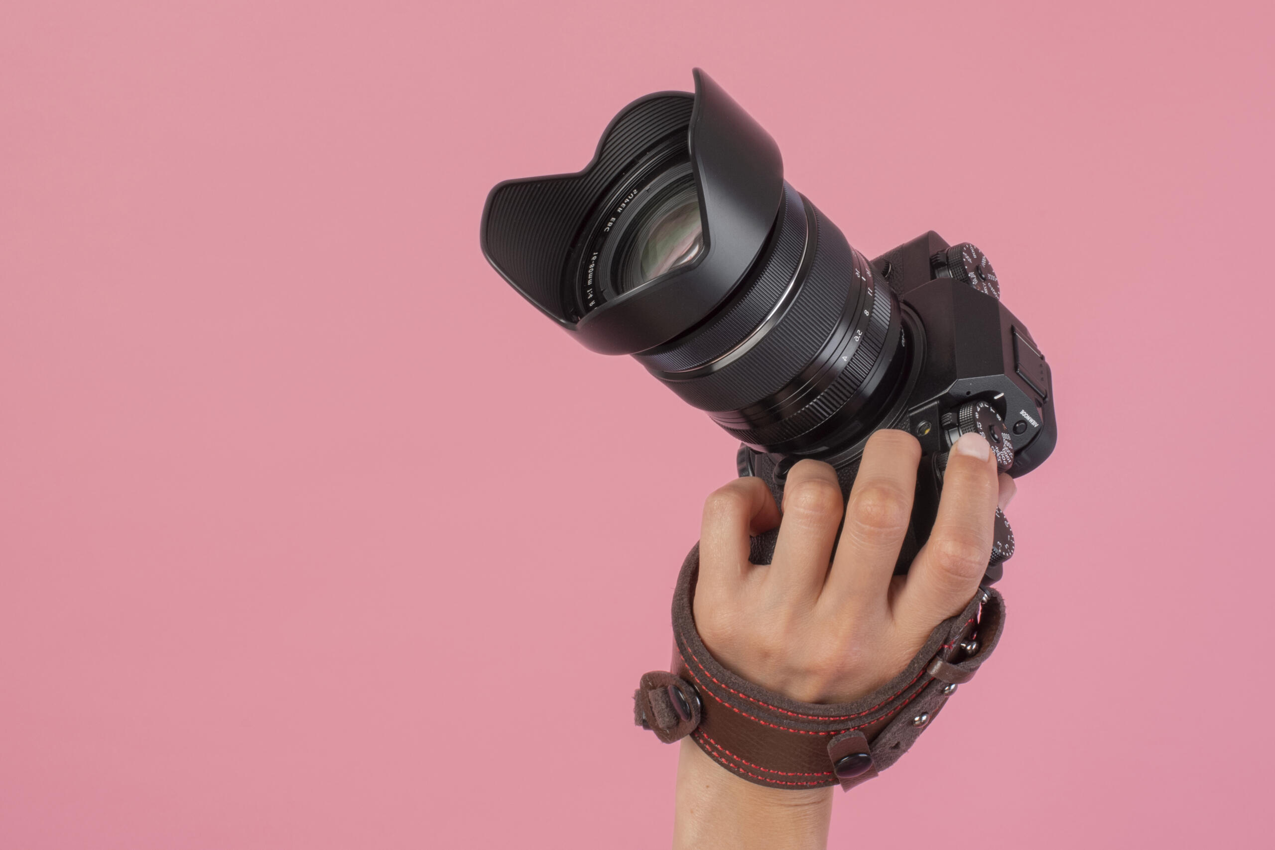camara reflex levantada de lado con una mano en un fondo rosado