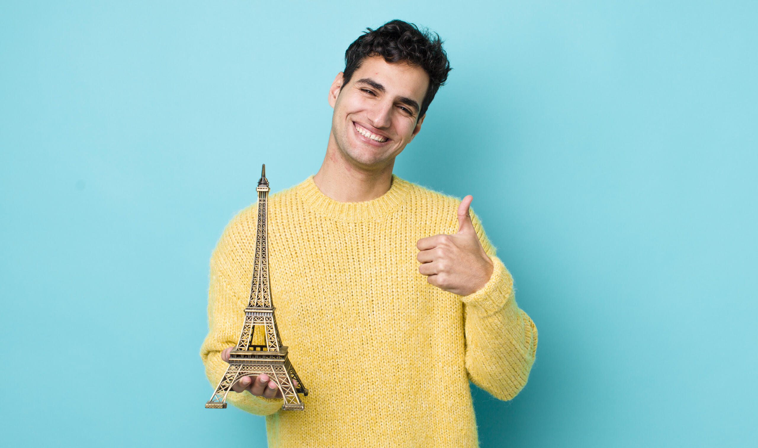 chico sonriente sosteniendo una torre eiffel en un fondo turquesa