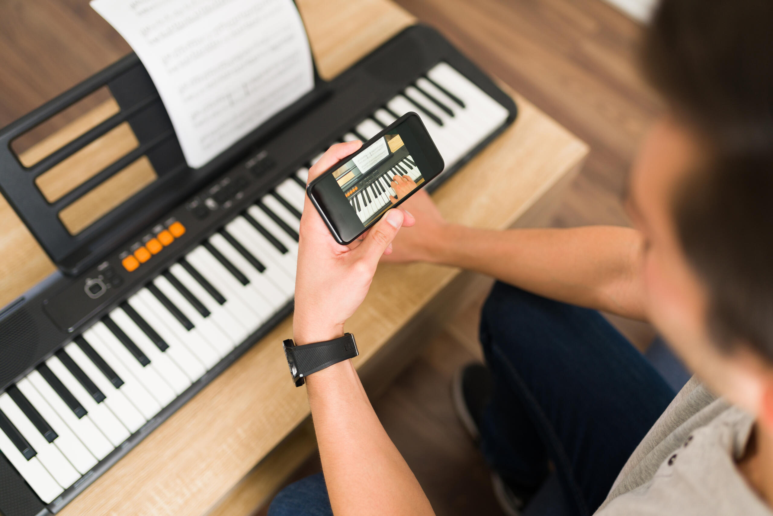 vista cenital de chico tocando un teclado electrónico mientras mira la guía de un video