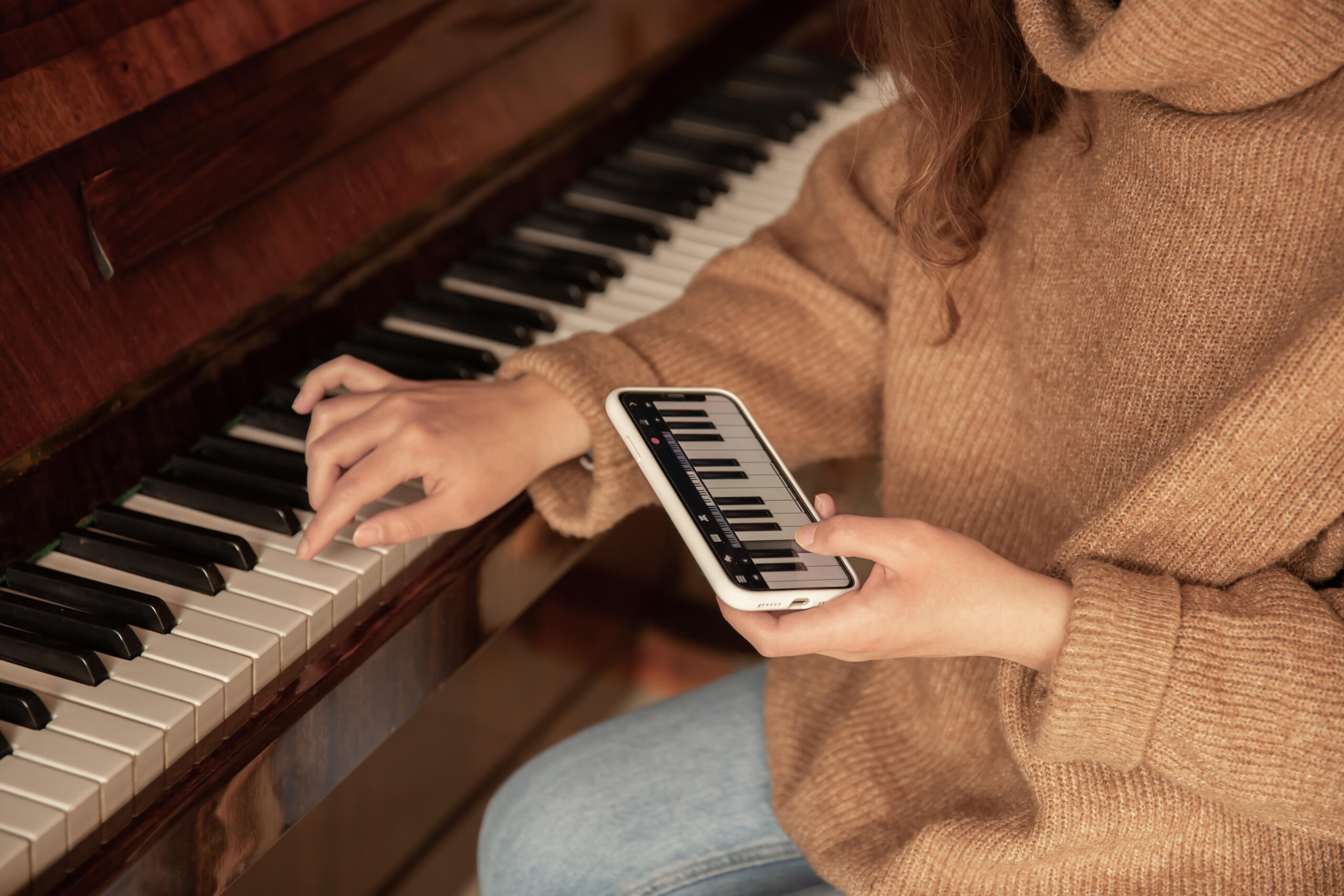 vista de manos de una mujer sentada frente a las teclas del piano siguiendo las notas que muestra su app de piano para aprender a tocar
