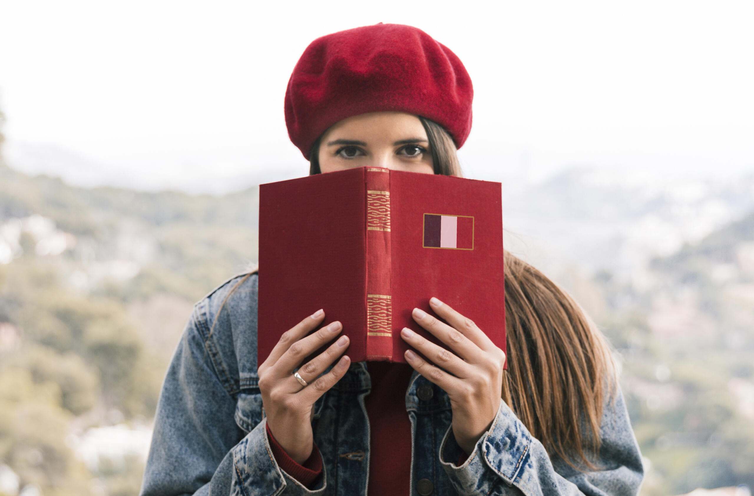 chica sosteniendo un libro de francés frente a su cara con solo sus ojos a la vista