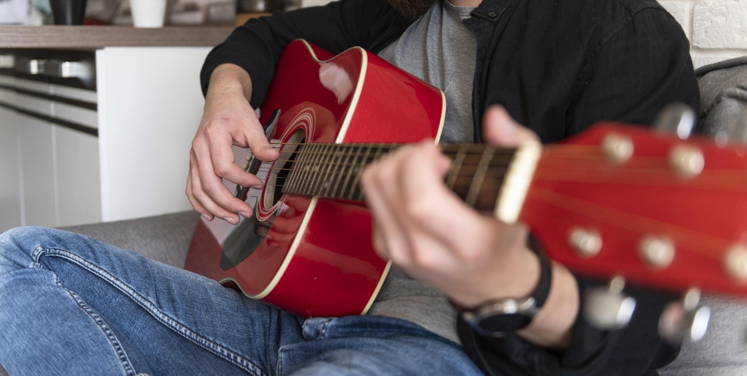foto de lado de una guitarra roja en medio con manos tocando las cuerdas