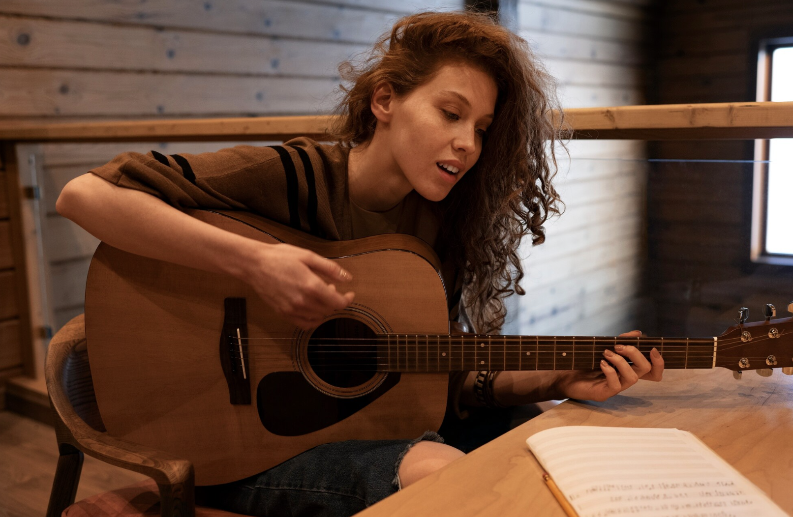 chica tocando la guitarra mientras lee unas partituras sobre la mesa