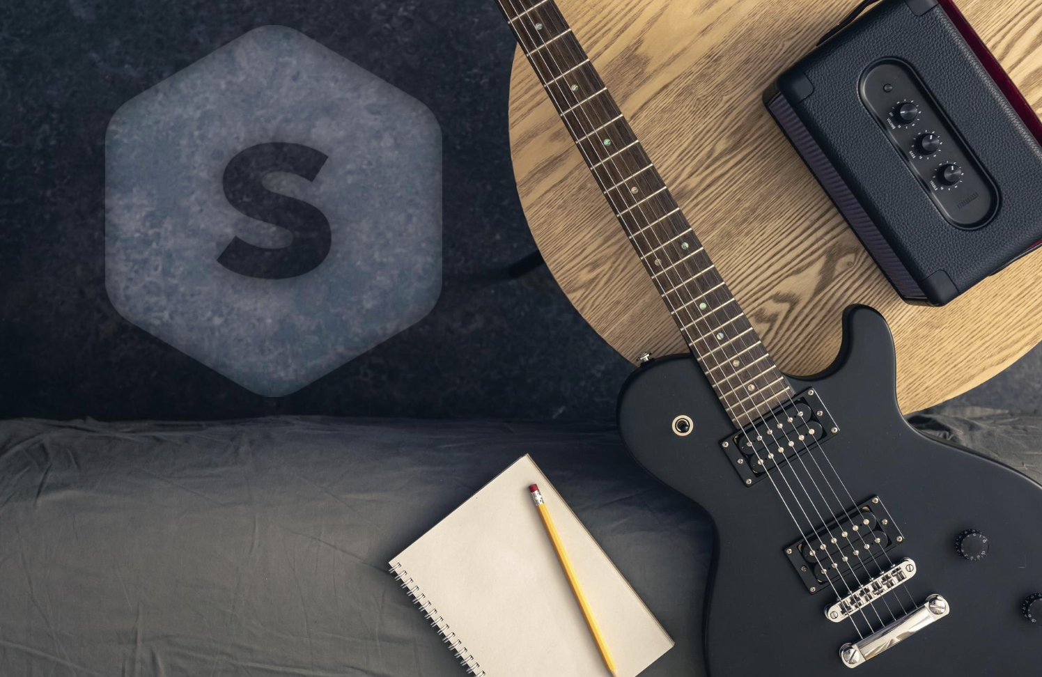 vista cenital de ambiente negro con una guitarra negra, cuaderno, lápiz y una grabadora con el logo de Superprof grabado en el piso