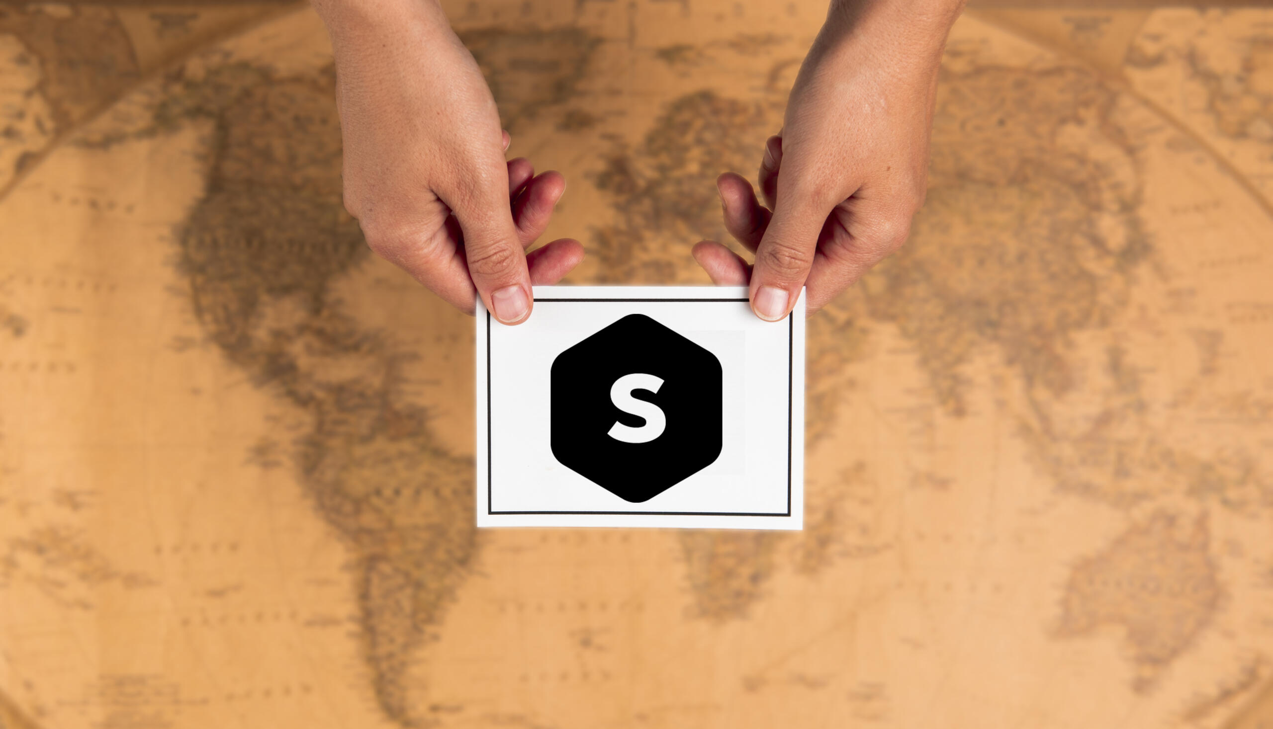 vista cenital de dos manos sosteniendo una carta con el logo de superprof sobre un mapa mundi