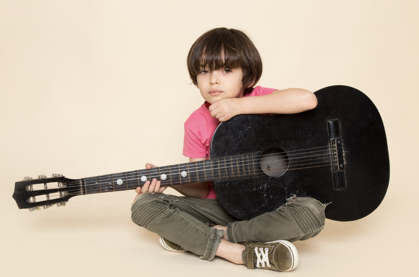niño pequeño sentado sosteniendo una guitarra negra con la mano y el menton apoyado en un lado del instrumento