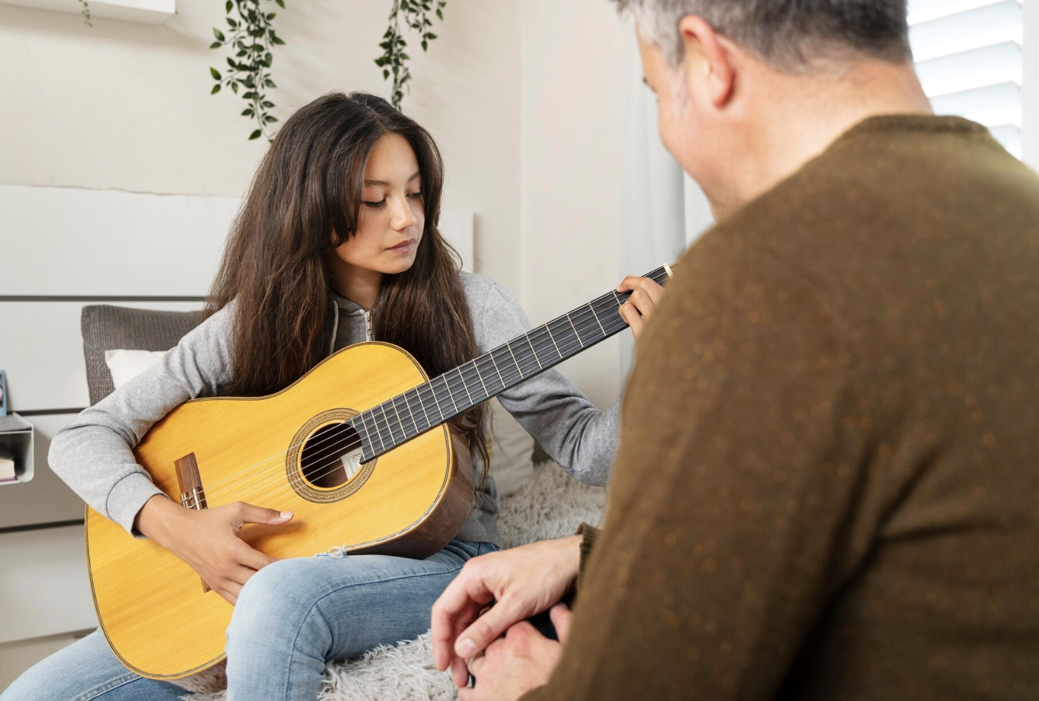 niña tocando una guitarra con profesor de espaldas a la cámara mirando como toca el instrumento