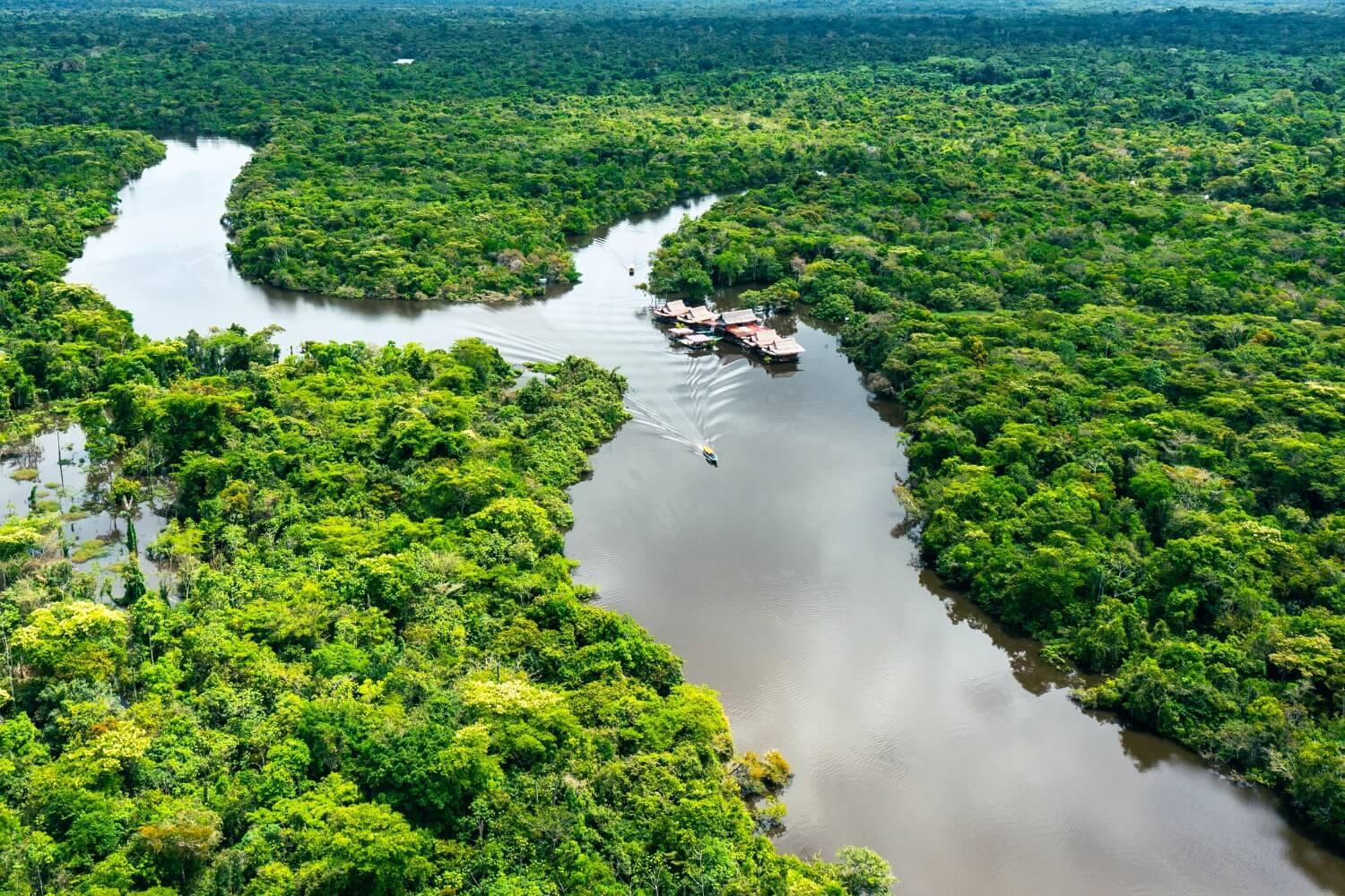 toma aerea de un fragmento del río amazonas con bosque tropical y unas embarcaciones navegando el rio
