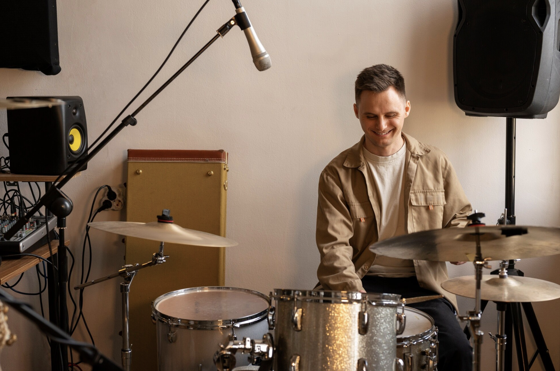 chico sonriente tocando la bateria en un estudio con micrófono y equipos de grabación