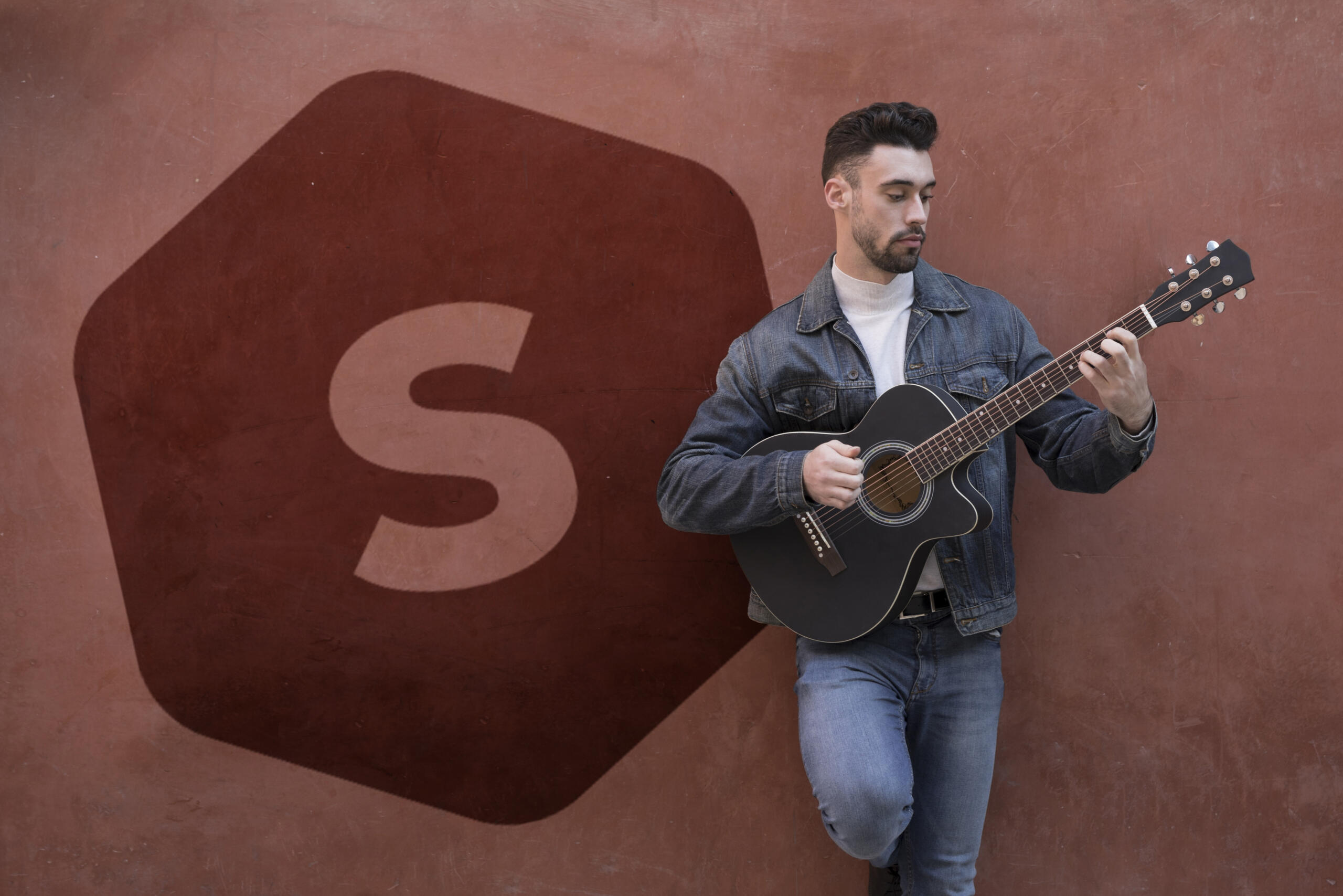 chico con una guitarra apoyado en un muro con el logo de superprof