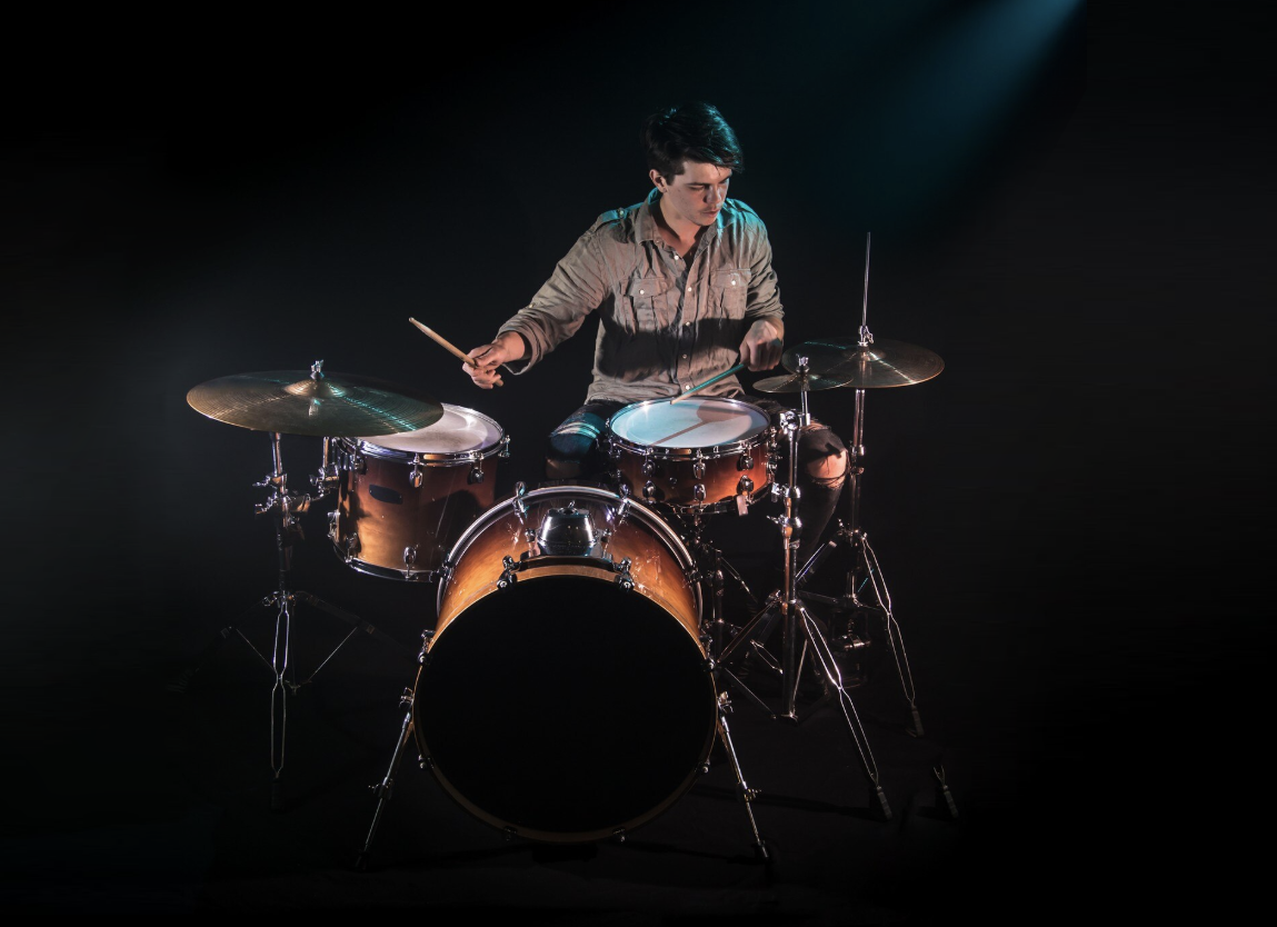 chico tocando la bateria en medio de un escenario completamente negro