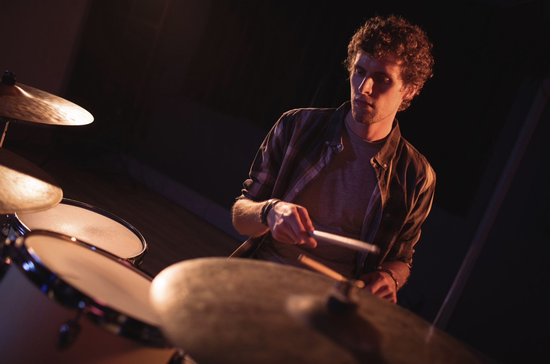 chico tocando la bateria en un escenario de luces cálidas