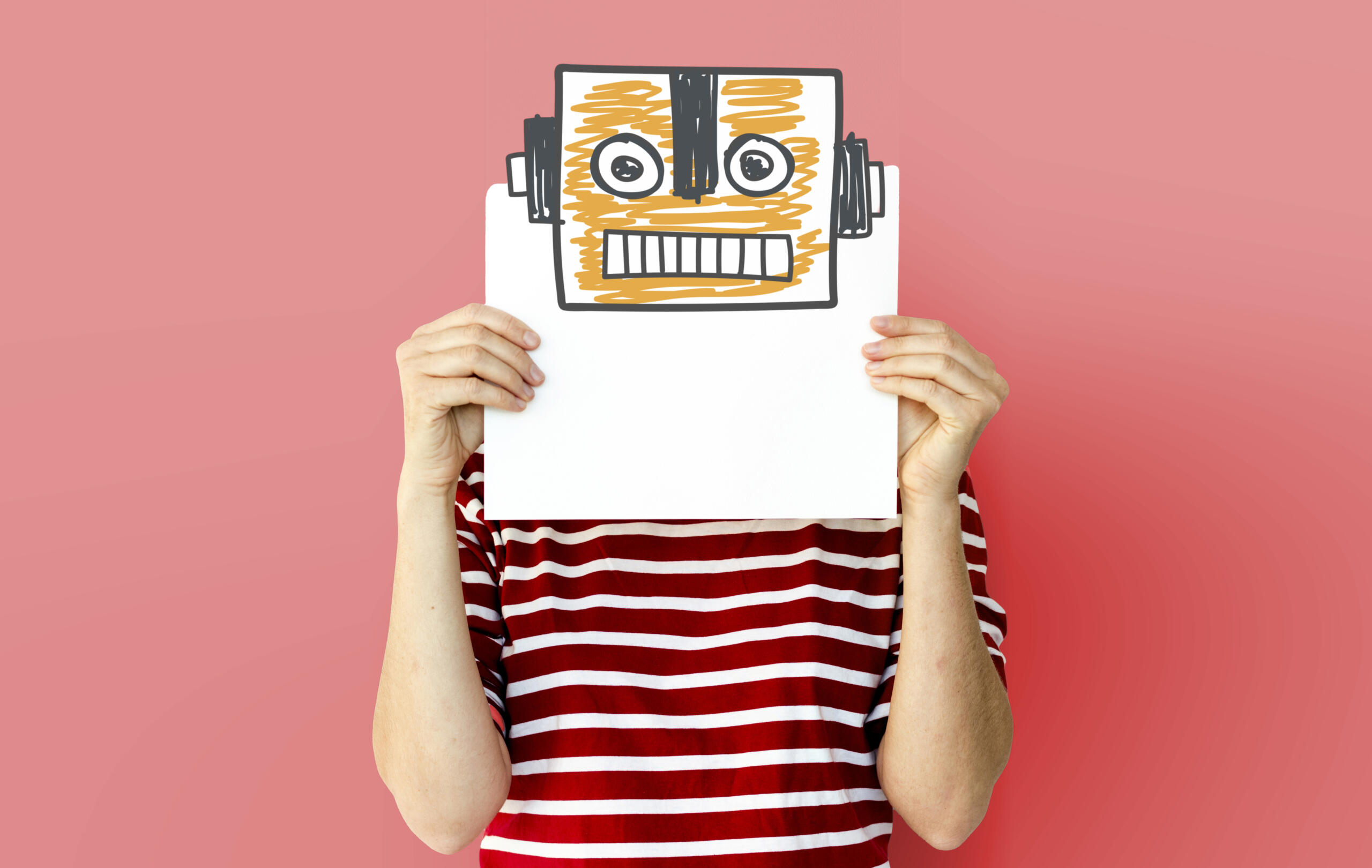 chico sosteniendo una hoja sobre su cara con el dibujo de una cabeza de robot