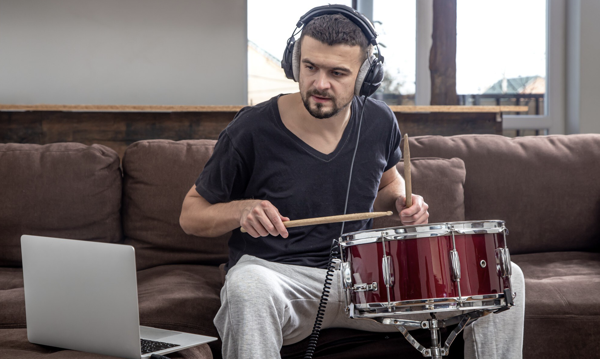chico sentado en un sofa tocando batería con audifonos frente a una laptop