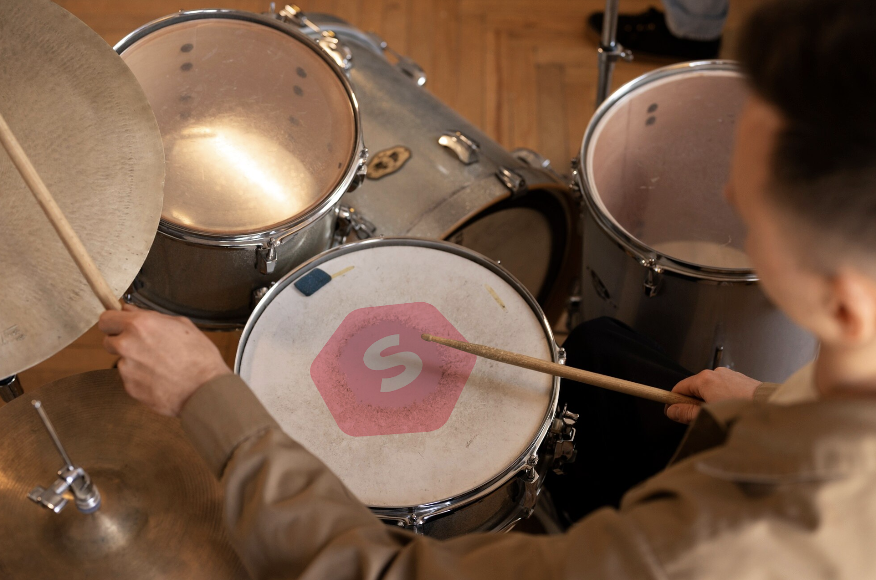 vista contrapicada de chico tocando la bateria y logo de superprof en el centro del tambor