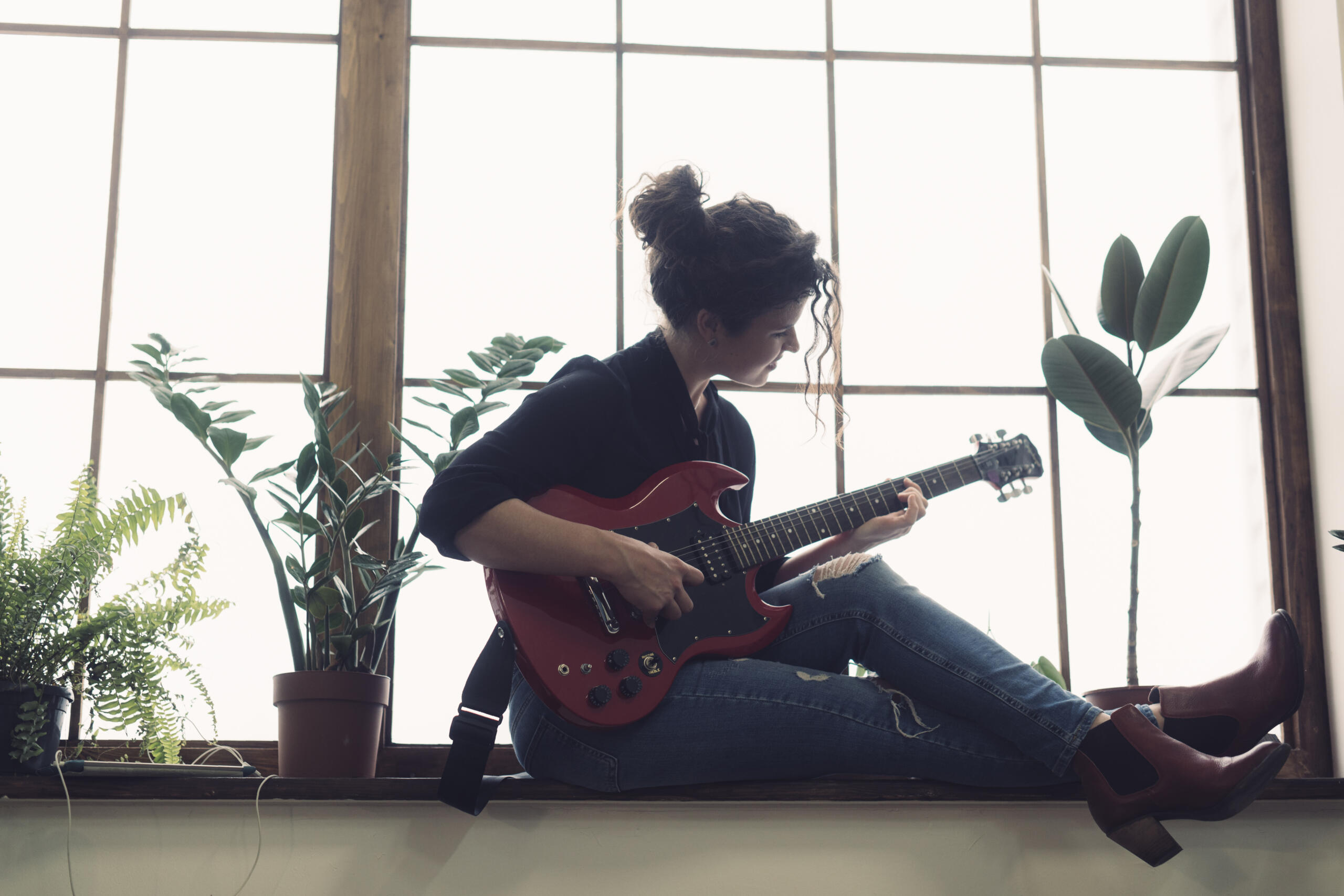 chica tocando una guitarra eléctrica sentada en el borde de un gran ventanal