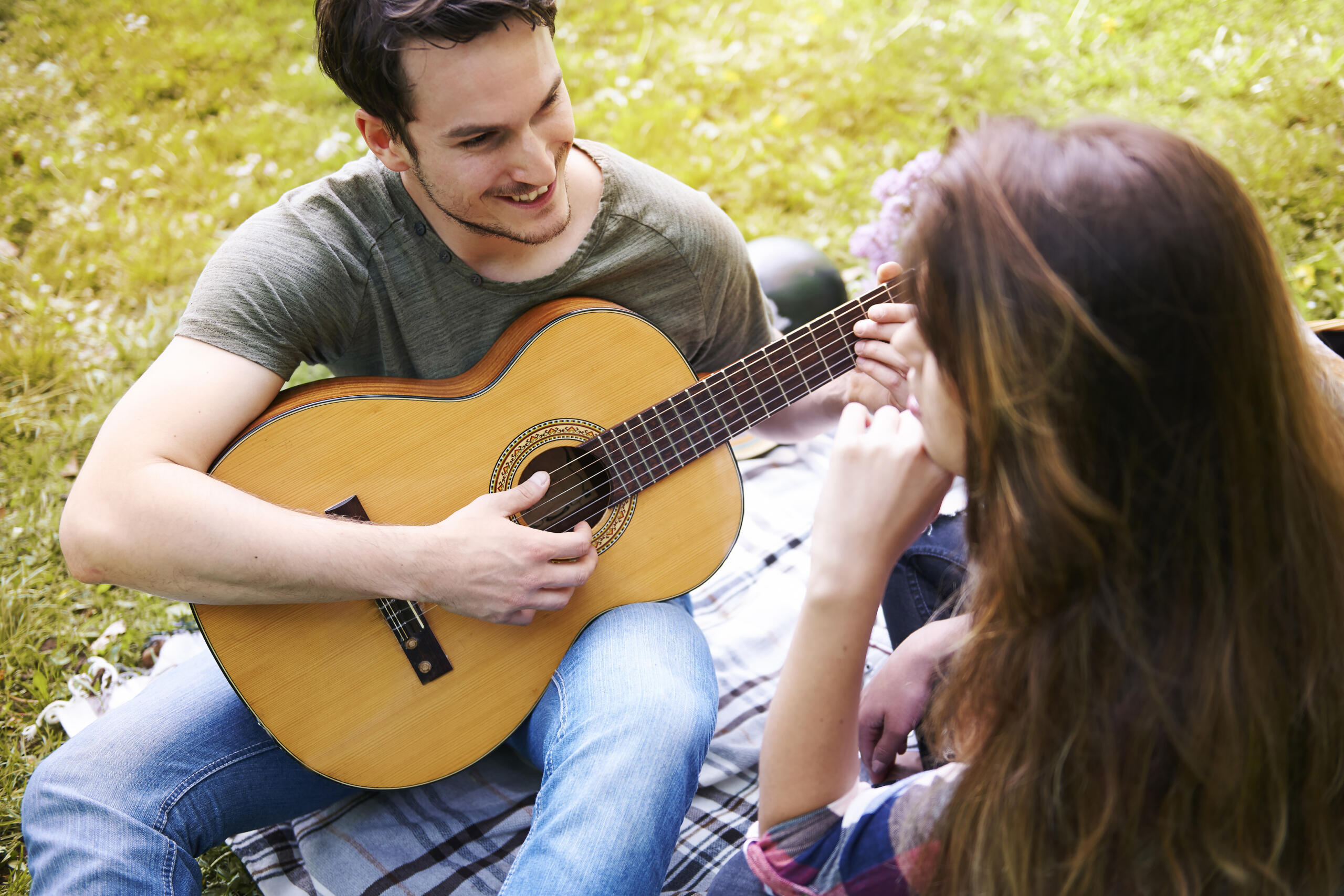 chico y chica sentados en un jardín sonrientes mientras el chico toca la guitarra