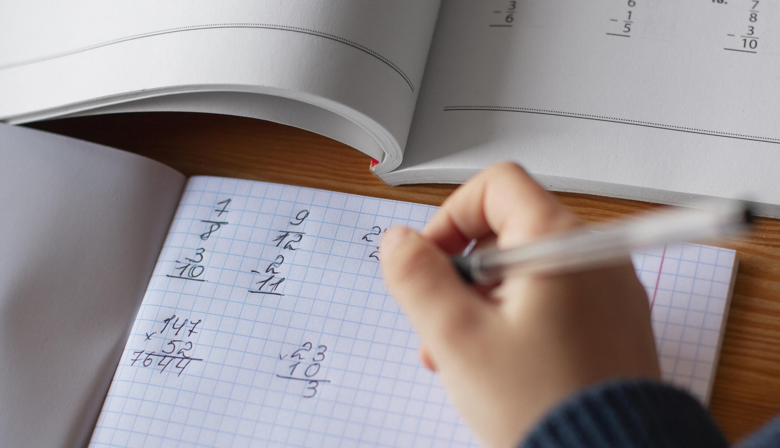 mano con libro junto a cuaderno de ejercicios de matemáticas