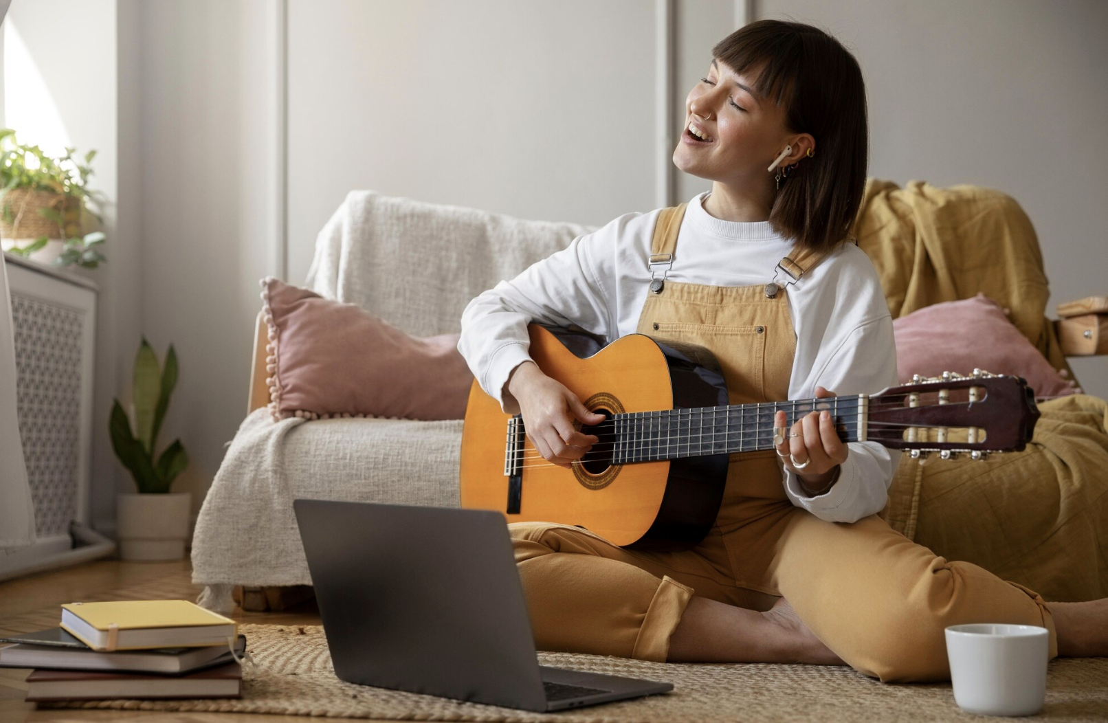 chica sonriente tocando la guitarra con los ojos cerrado en la alfombra frente a una laptop