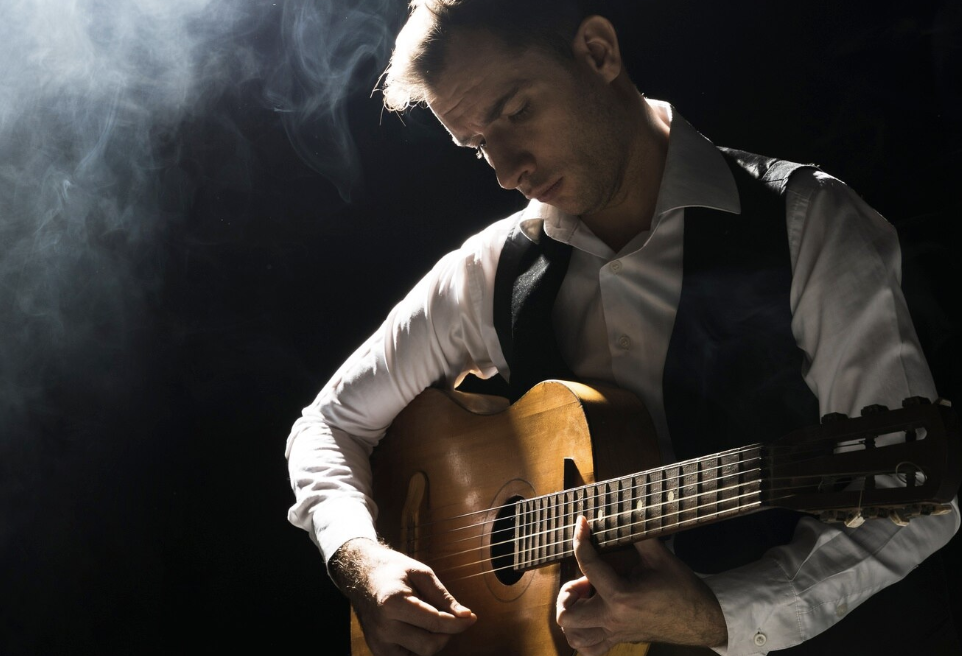 chico con ropa formal tocando una guitarra con el reflector de un escenario iluminándolo