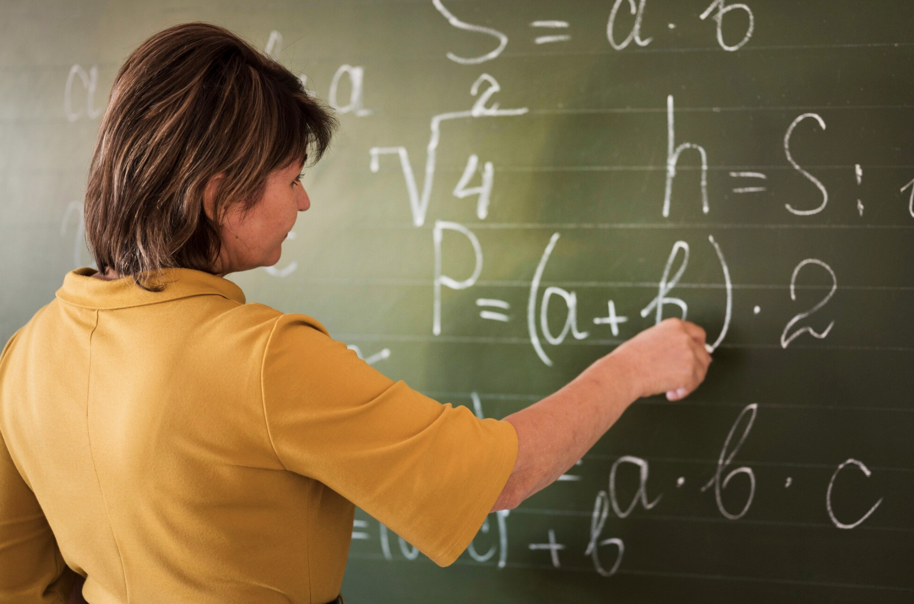 profesora resolviendo formulas matemáticas en la pizarra verde
