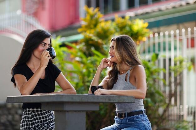 dos chicas conversando mientras toman una taza de cafe en una mesa