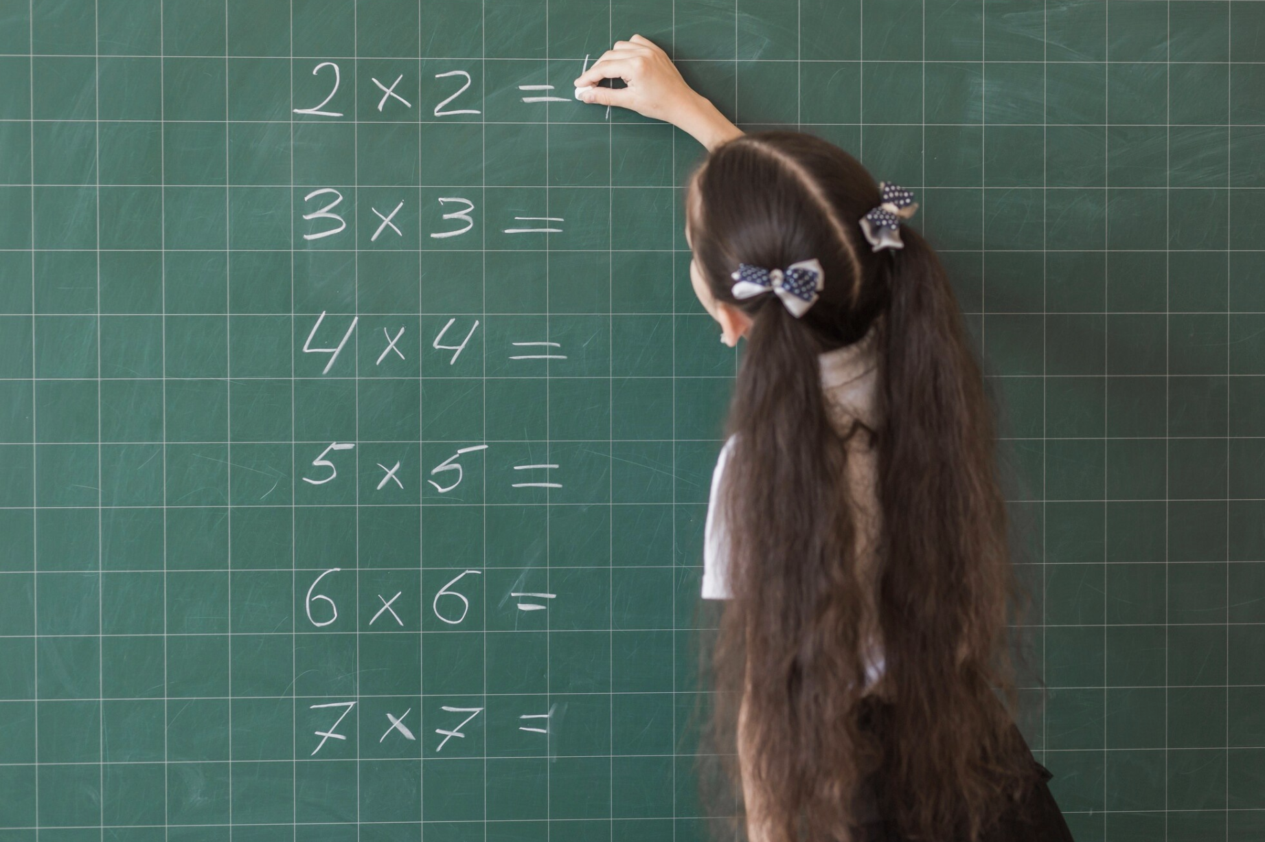 alumna con una tiza desarrollando ejercicios matematicos en pizarra verde