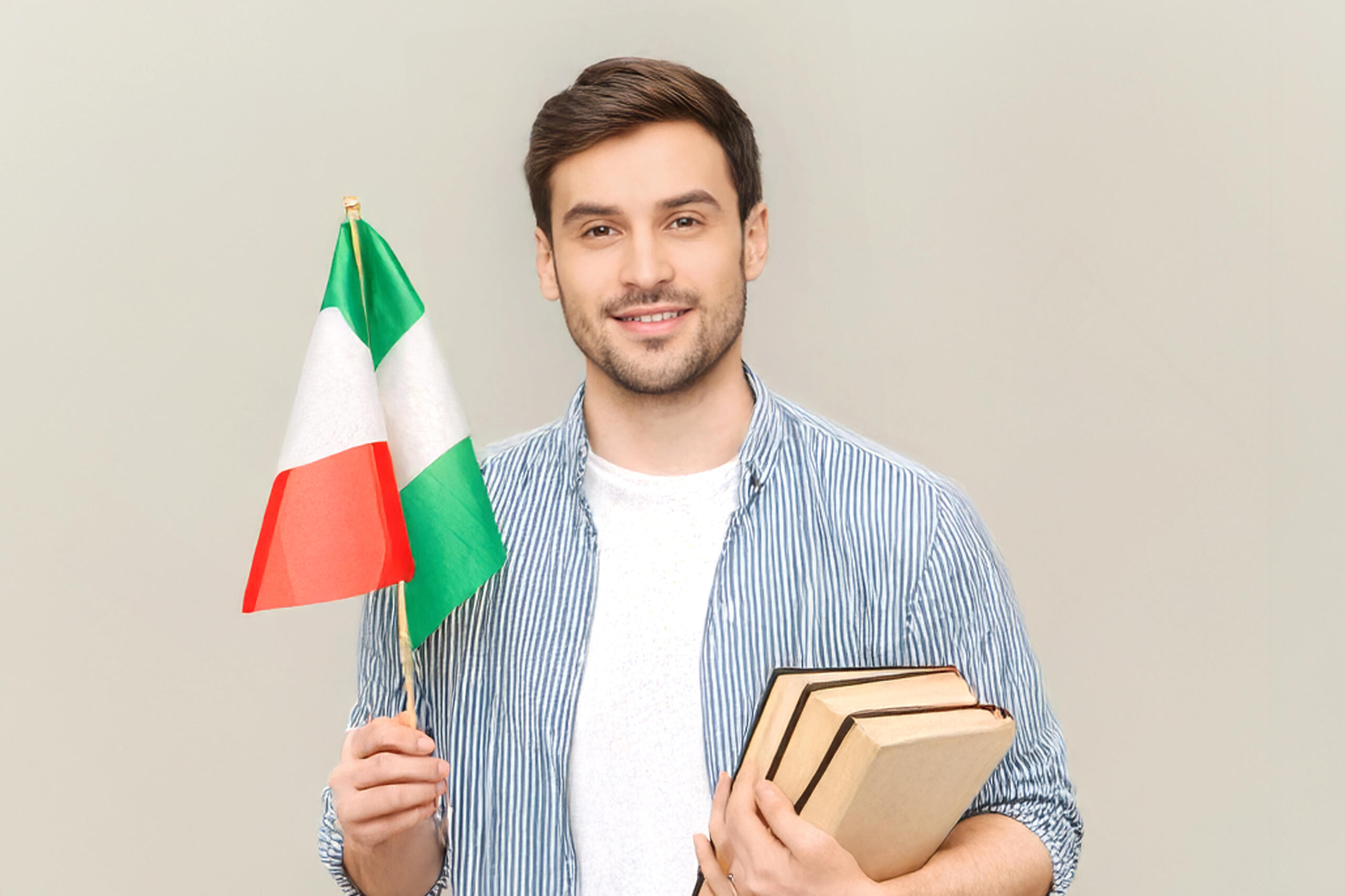 chico sonriente sosteniendo un banderin de italia y libros en la otra mano