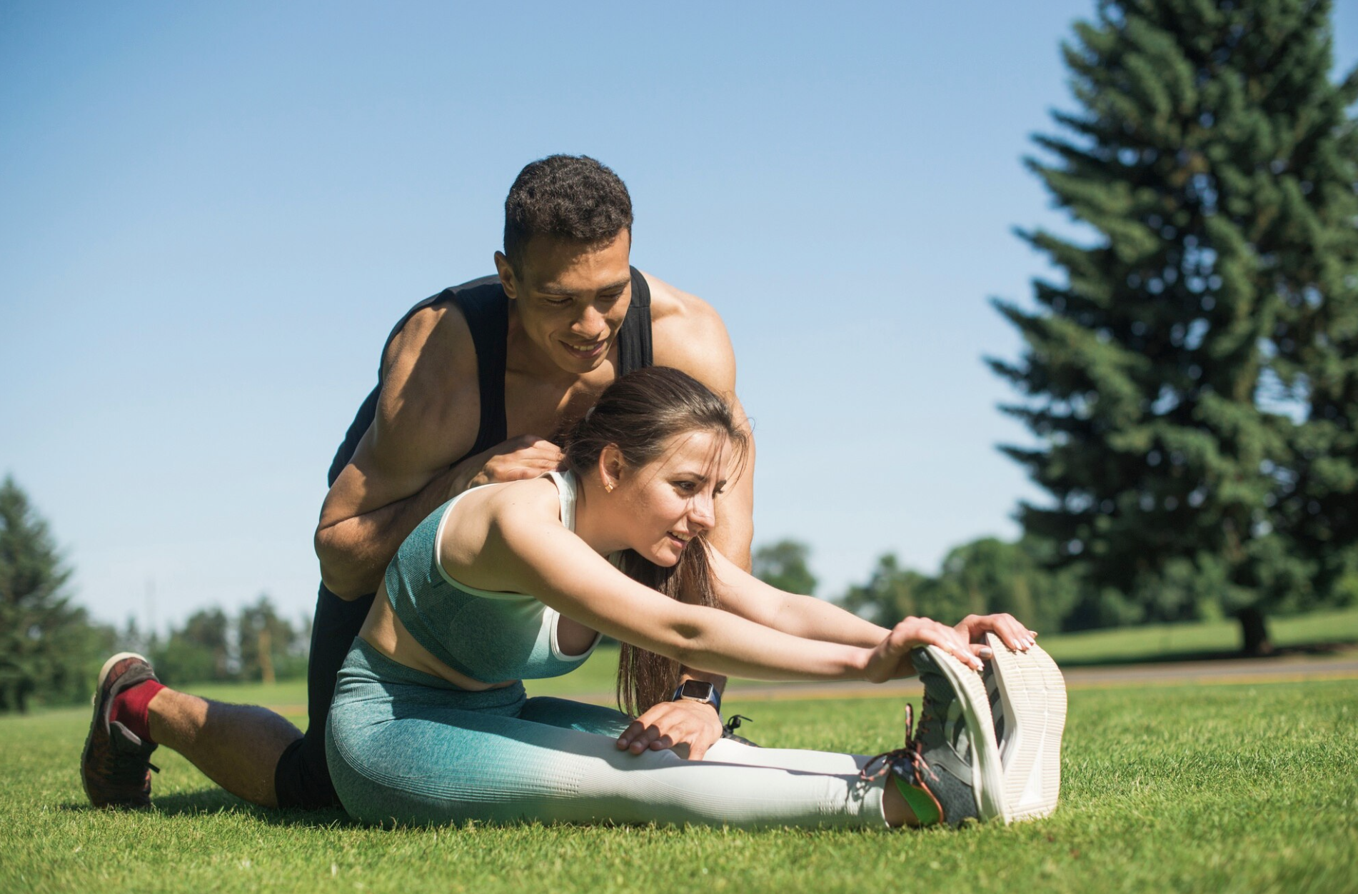 entrenador presionando la espalda para ayudar con el estiramiento de toque de puntas de los pies a una chica sentada en el jardin