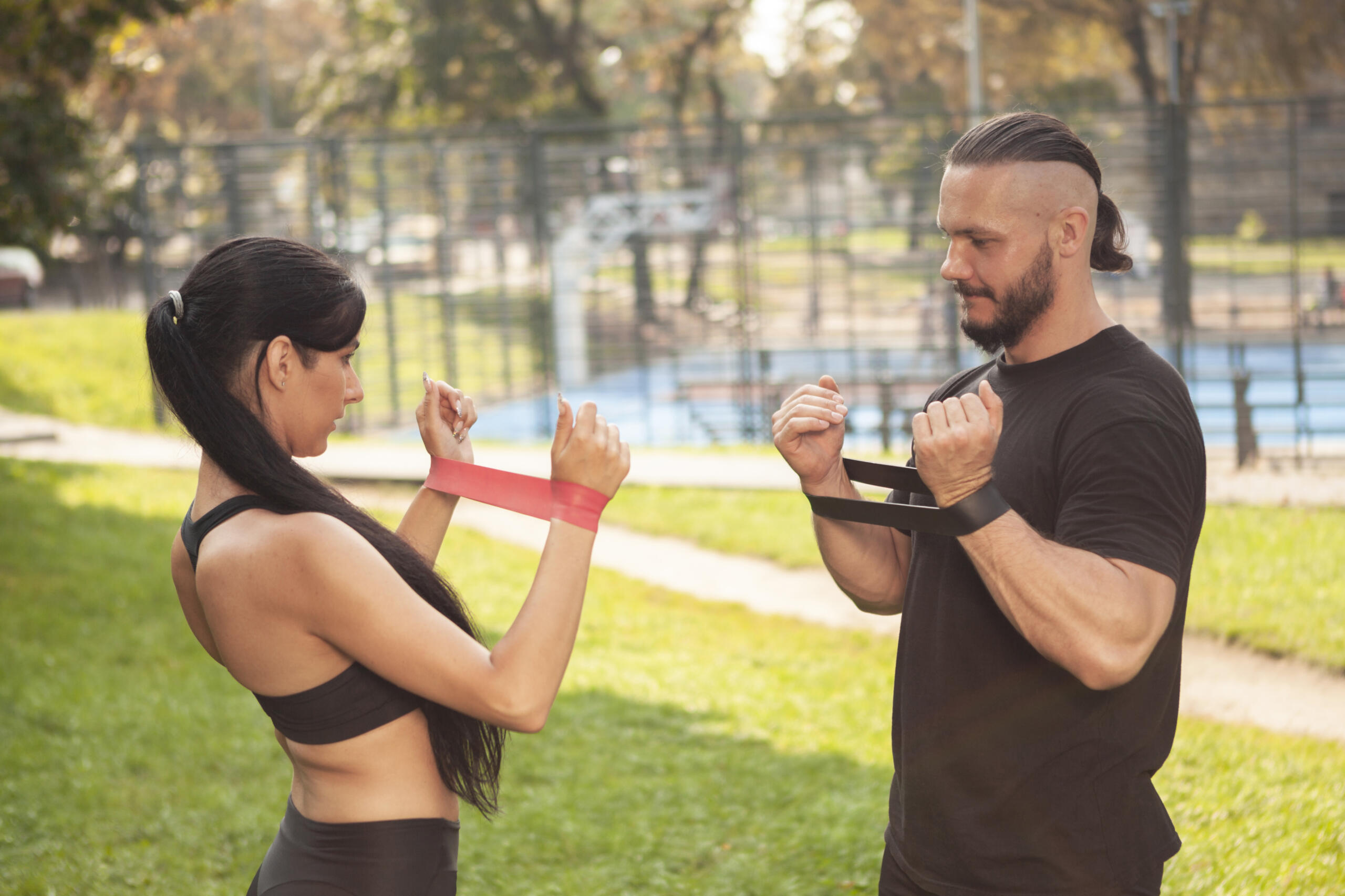 chico y chica entrenando frente a frente con ligas de ejercicios estiradas en las muñecas