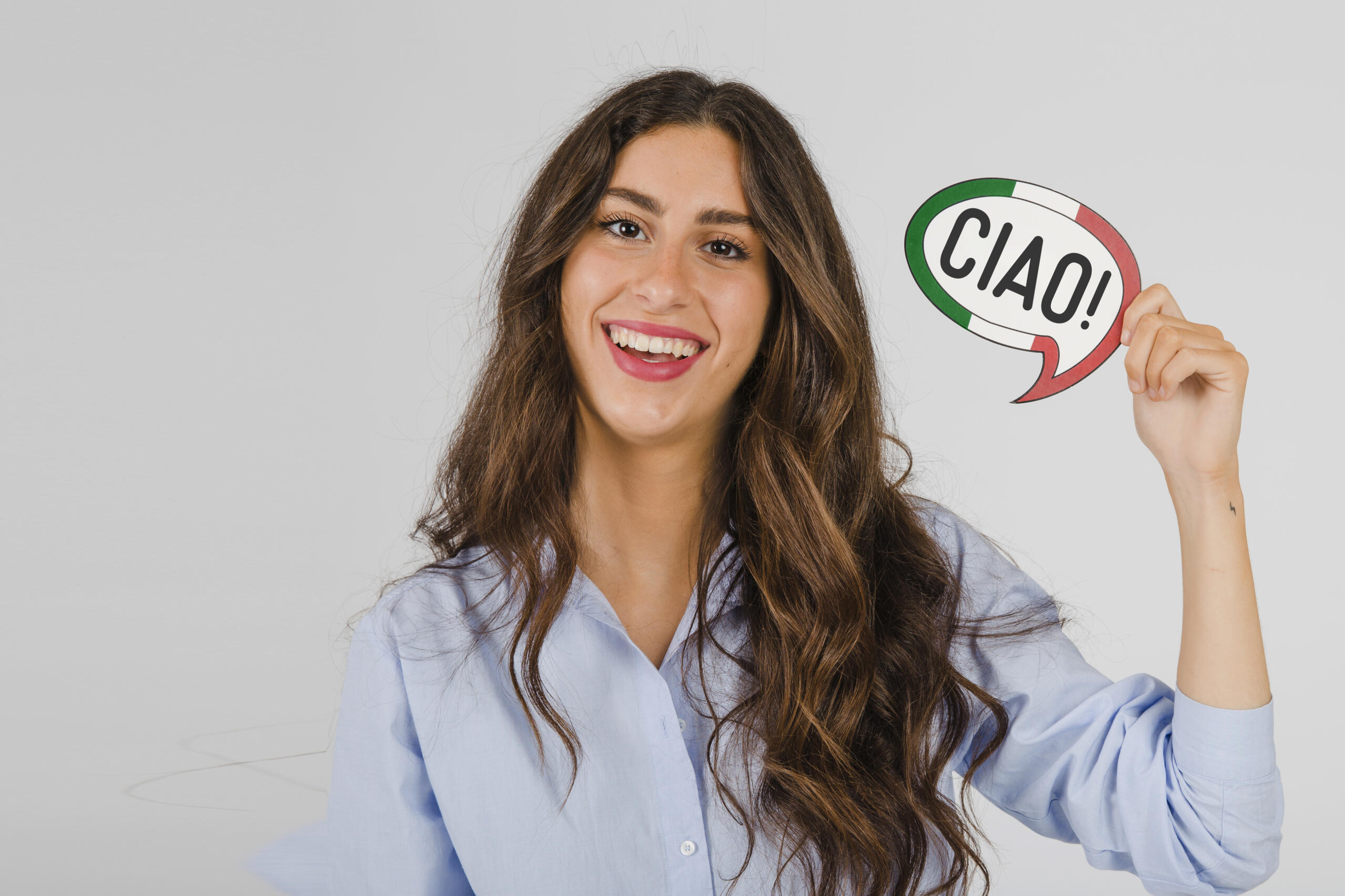 chica sonriente sosteniendo un cartel pequeño con los colores de la bandera italiana y la palabra CIAO! escrita en medio