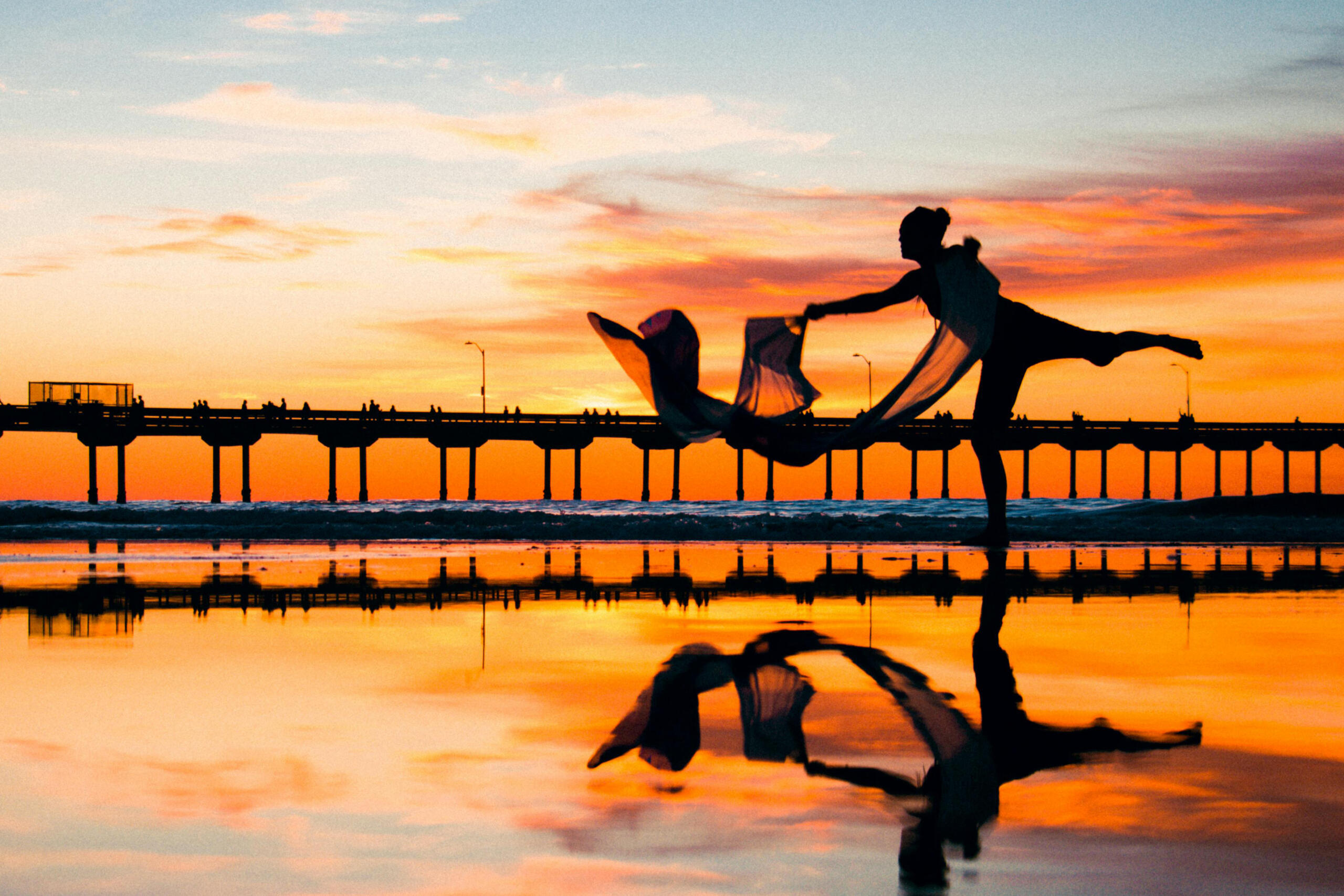 silueta de bailarina en un muelle con su reflejo en el mar y un atardecer