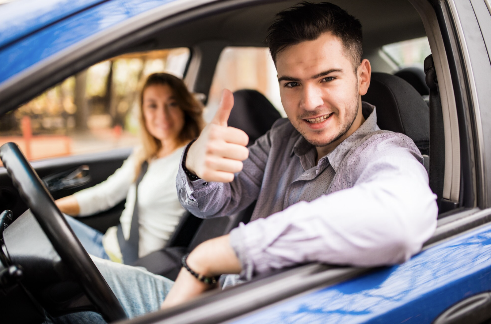chico sonriente haciendo un ok a la camara con la mano y su instructora de manejo de fondo