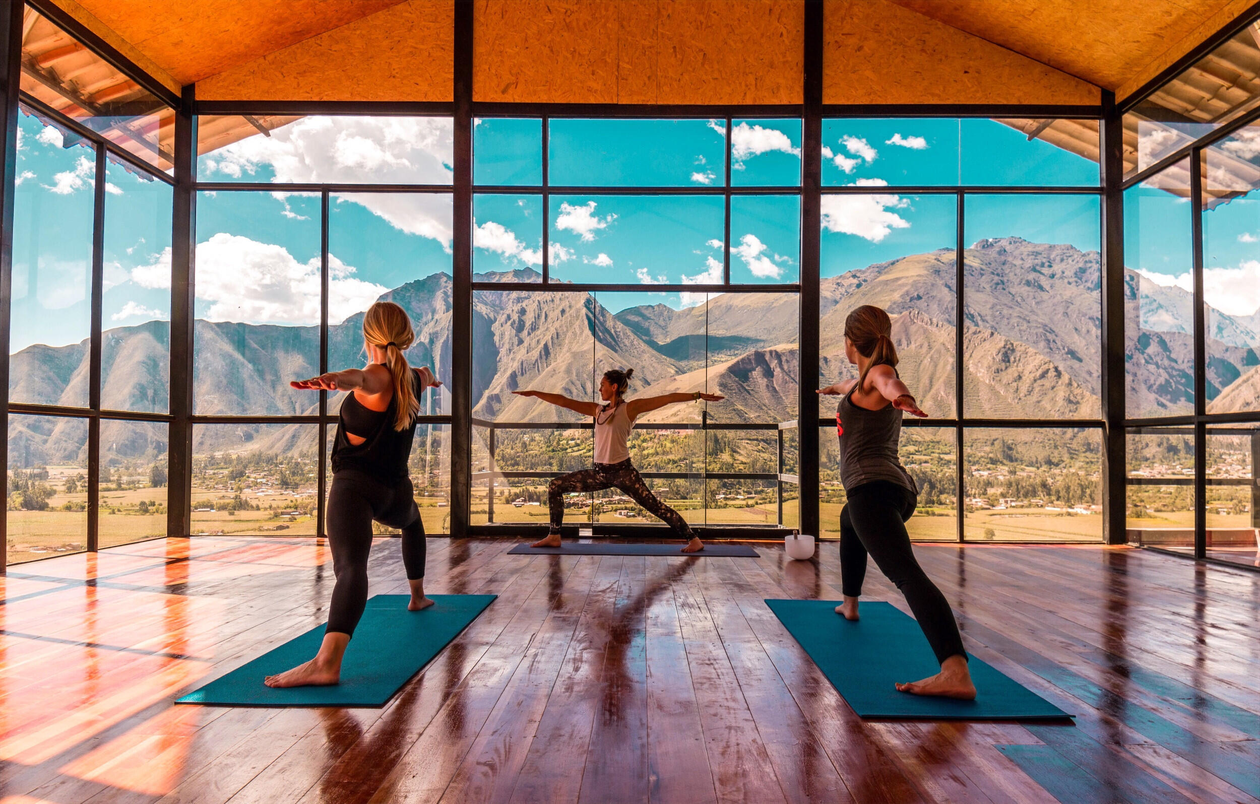 grupo de mujeres haciendo yoga frente a un ventanal con vista a las montañas