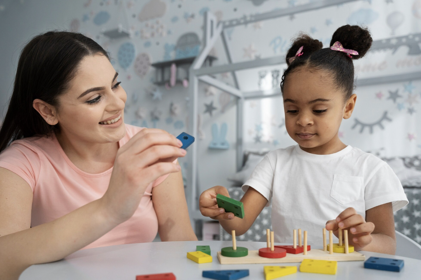 niña jugando con su maestra a un juego montessori de armar torres con piezas de diferentes formas y colores