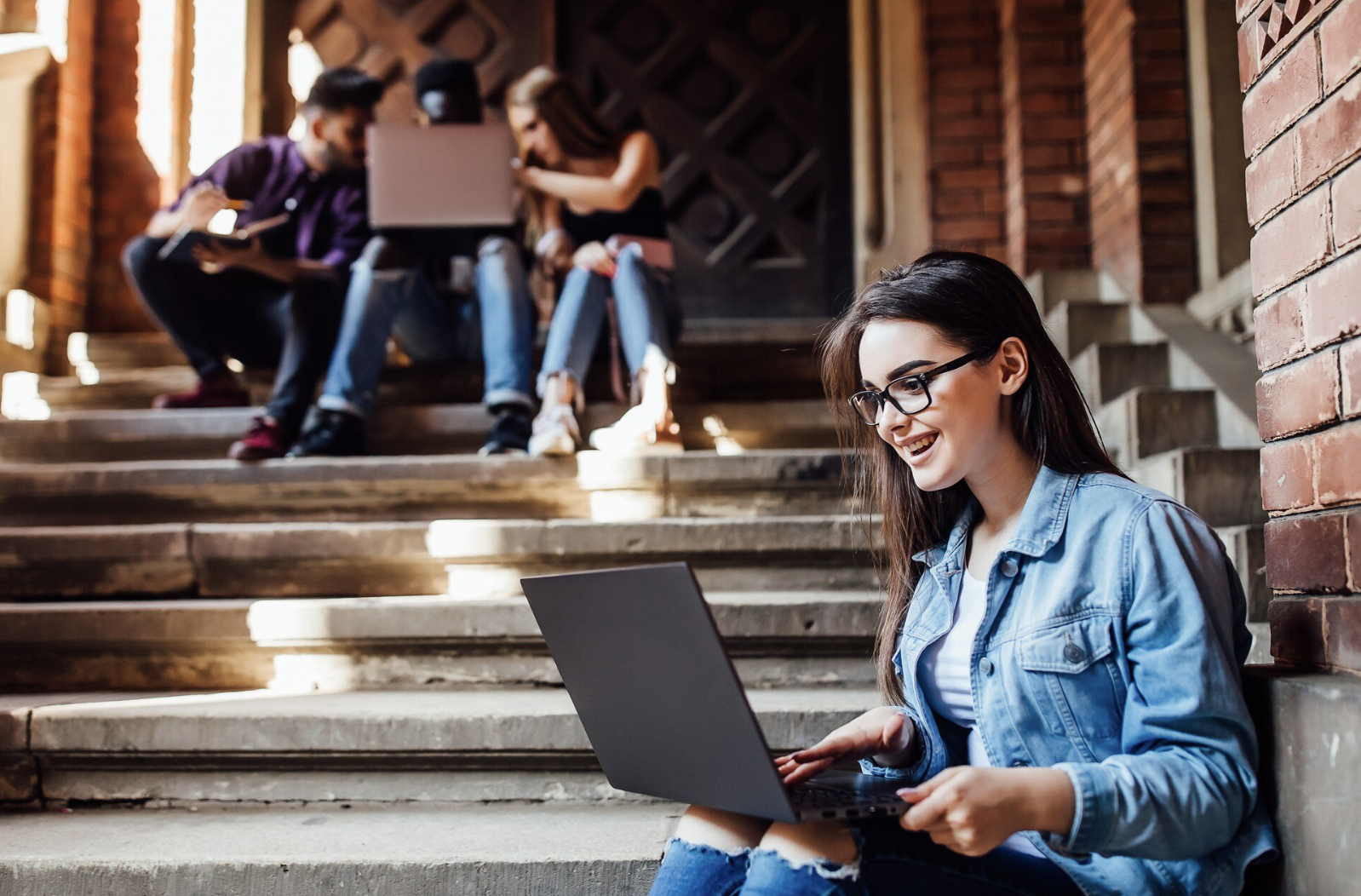 chica sonriente mirando su laptop sentada en las gradas de un pasillo universitario