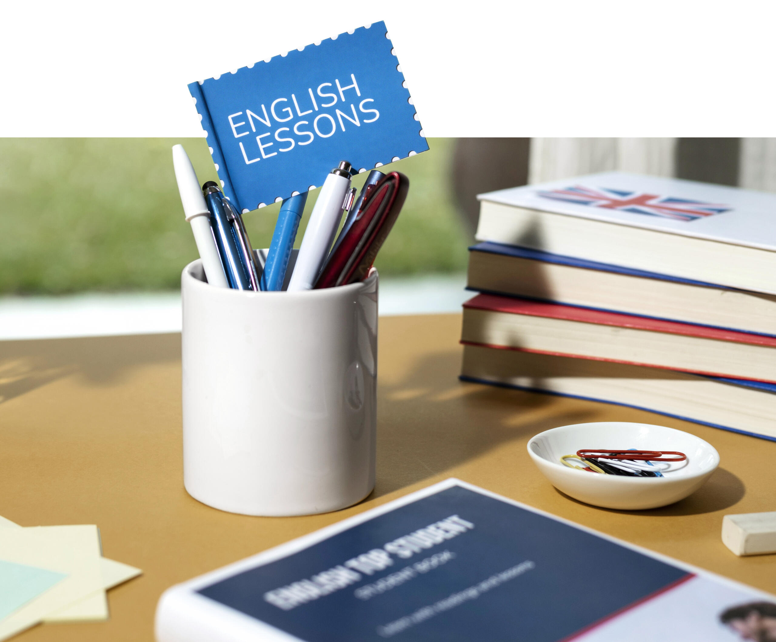 toma detalle de un escritorio con un portalapiceros con banderita ENGLISH LESSONS en medio con libros alrededor.
