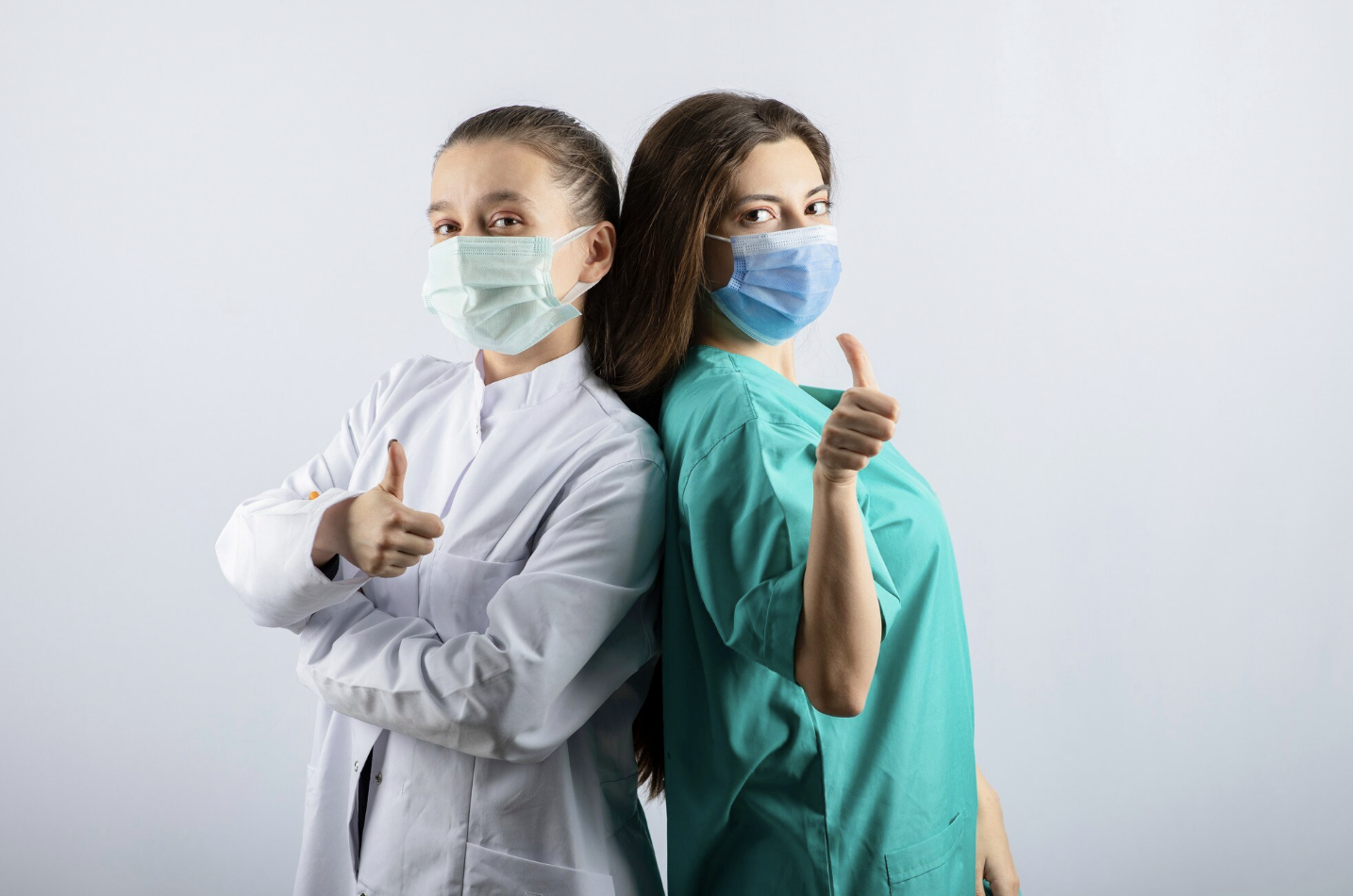 dos mujeres de carrera medica contra espaldas y mascarillas con un dedo mostrando ok