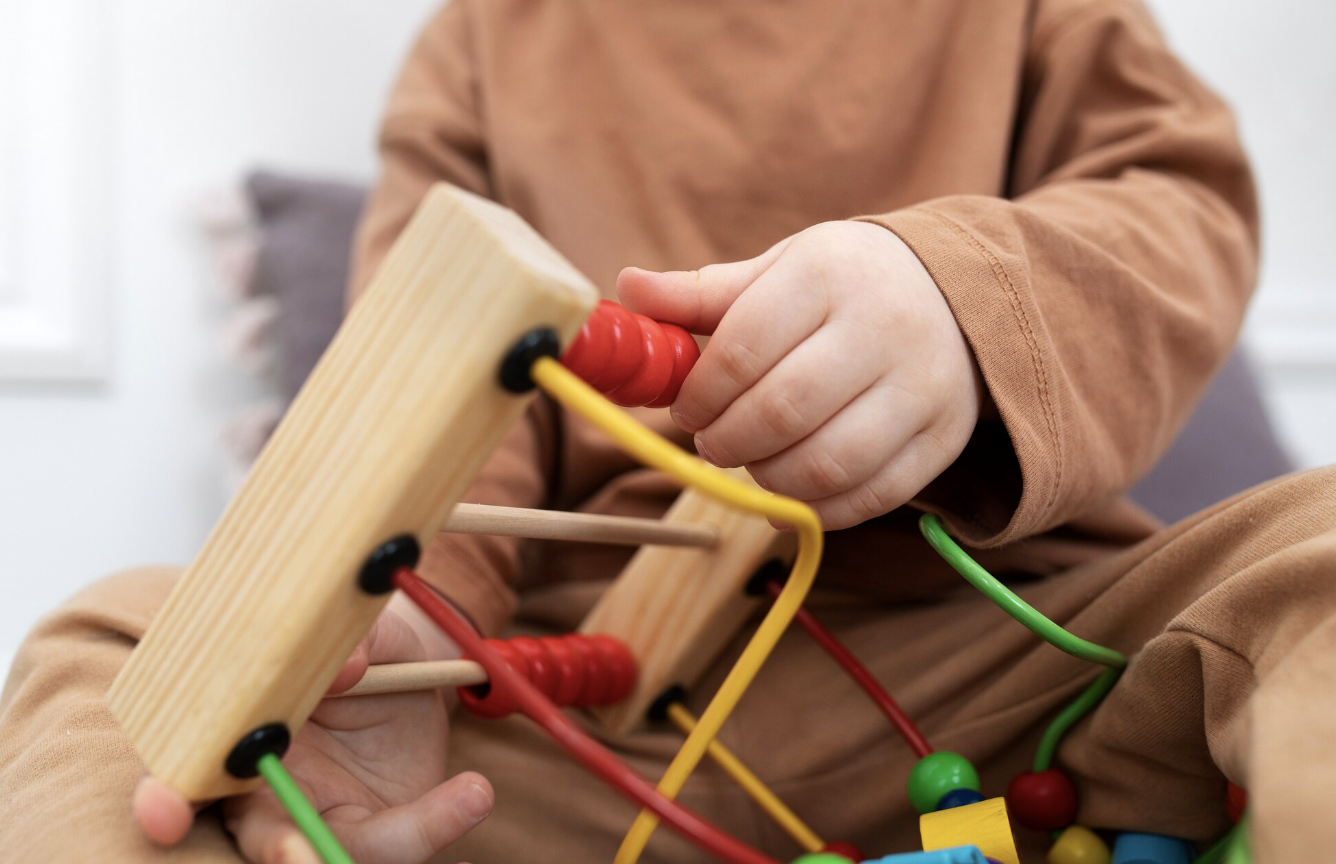 toma detalle de un niño pequeño sujetando entre sus manos un juguete montessori con cuentas de madera de colores y canales por los que se mueven