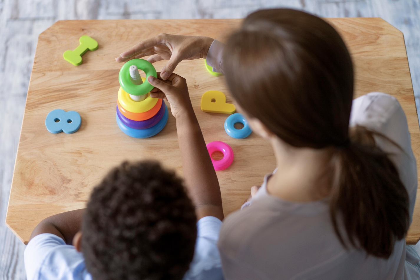 toma cenital de mama junto a su hijo jugando sobre una mesa de madera con un juguete de torres Montessori
