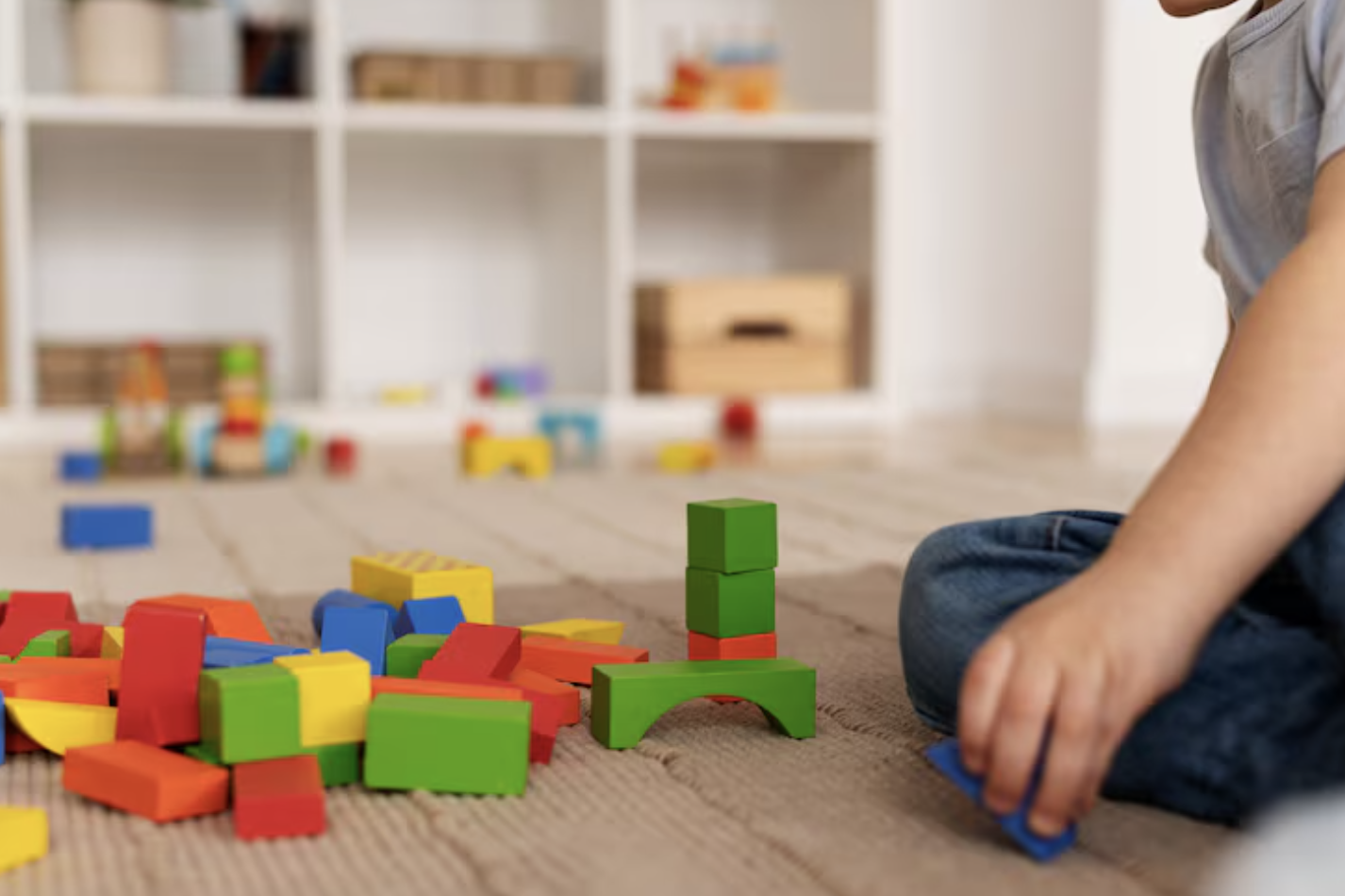 toma detalle de bloques de madera con diferentes formas y tamaño junto a mano de un niño que está jugando con las piezas