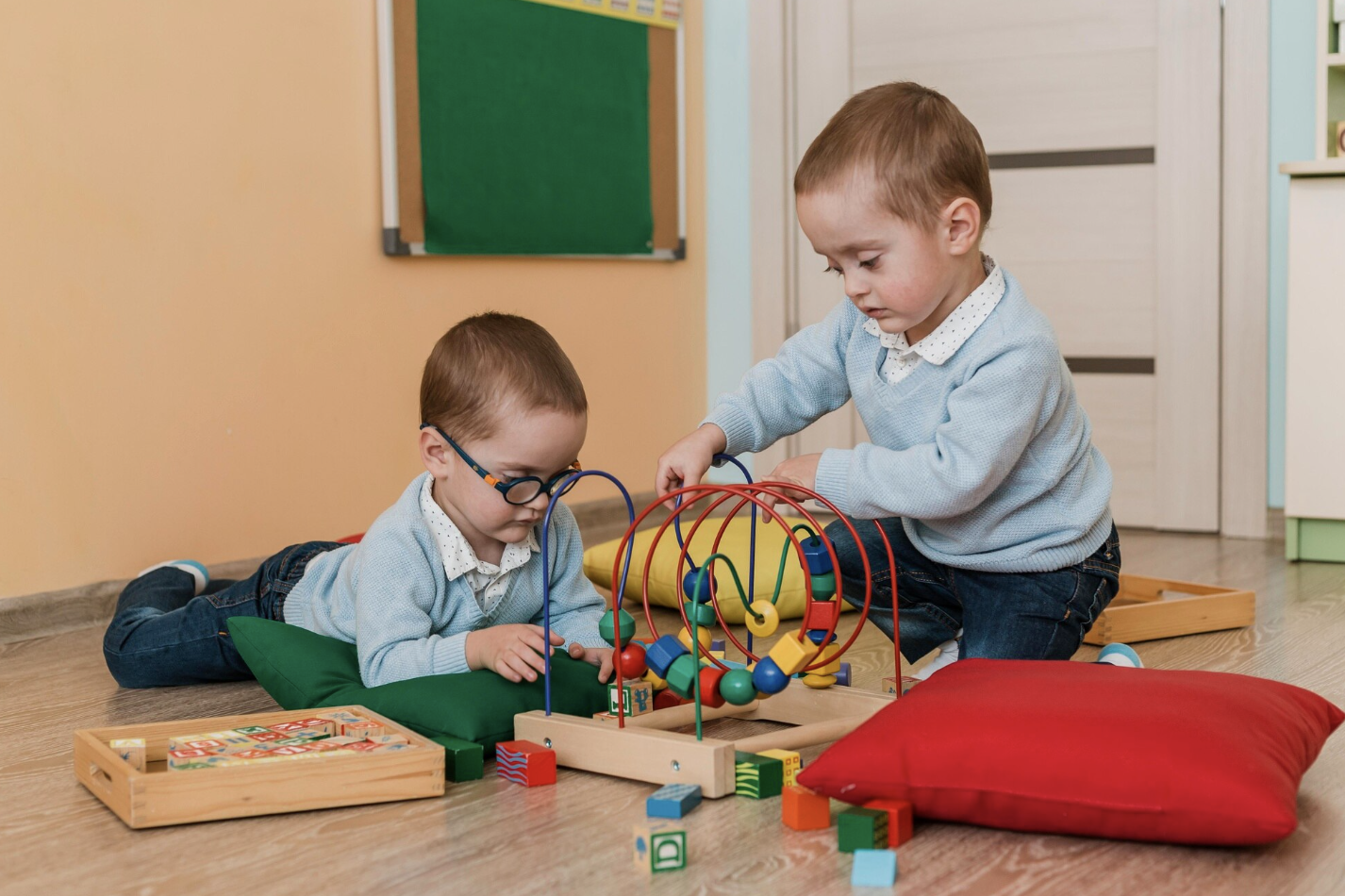 dos niños pequeños en el suelo de un aula jugando con juguetes montessori