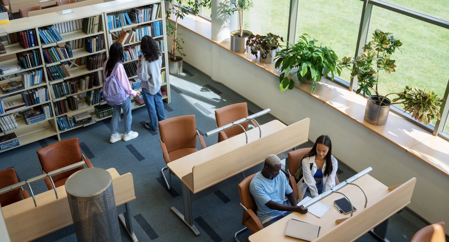 toma contrapicada de una biblioteca universitaria con cuatro alumnos sentados y en estanterias