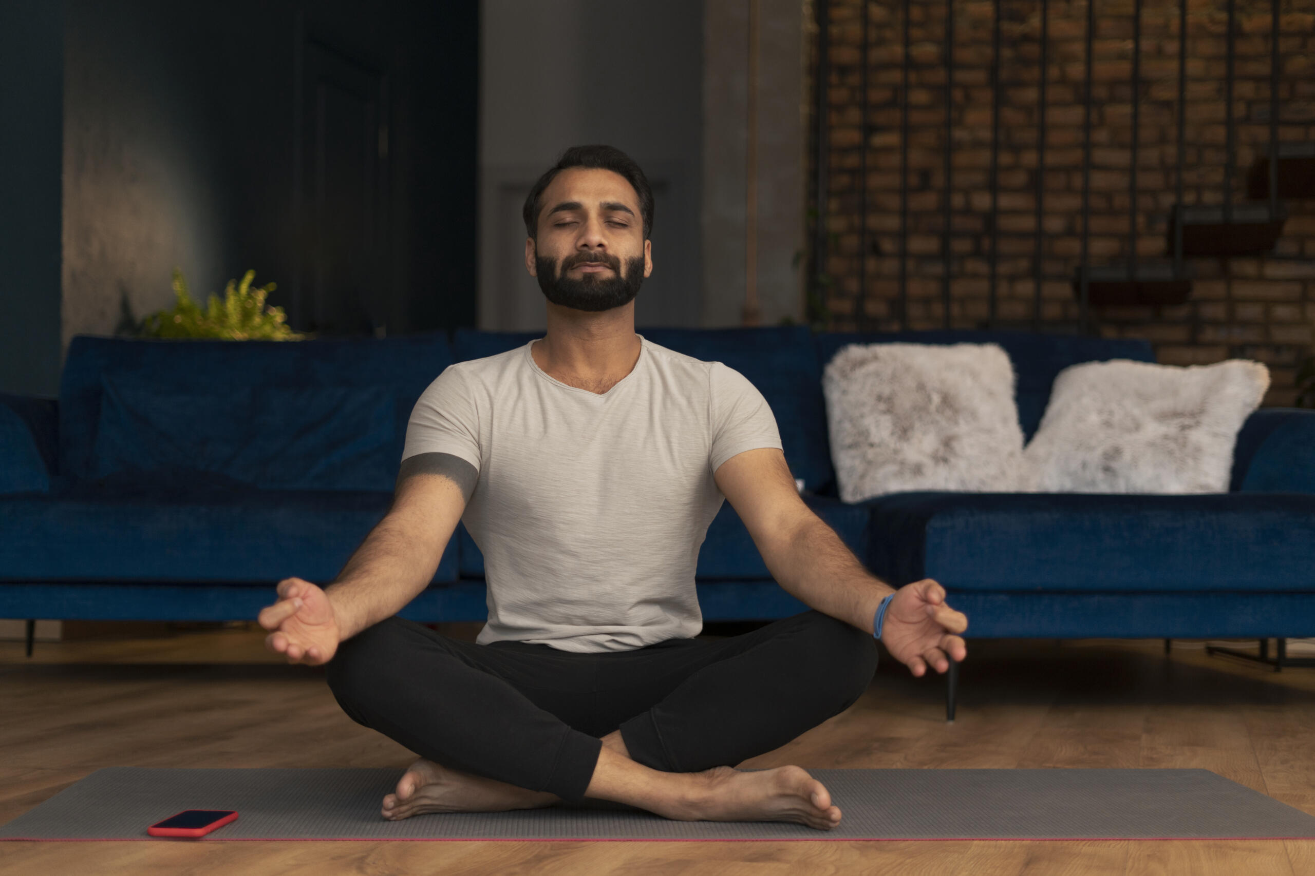 chico con los ojos cerrados en medio de la sala de su casa en posicion de meditacion sobre un mat